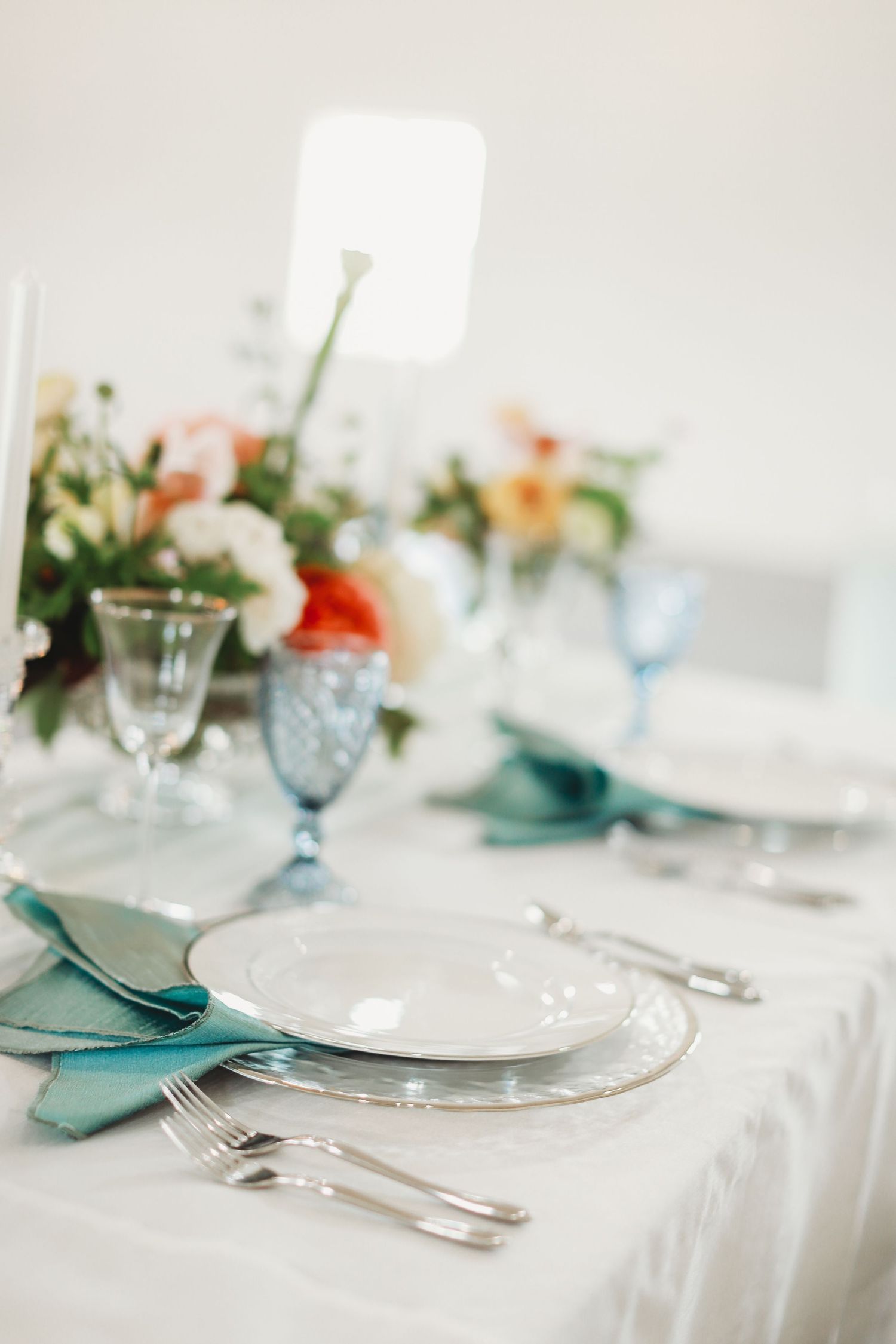 Elegant table setting with blue glassware, white linens, and coral floral centerpieces.