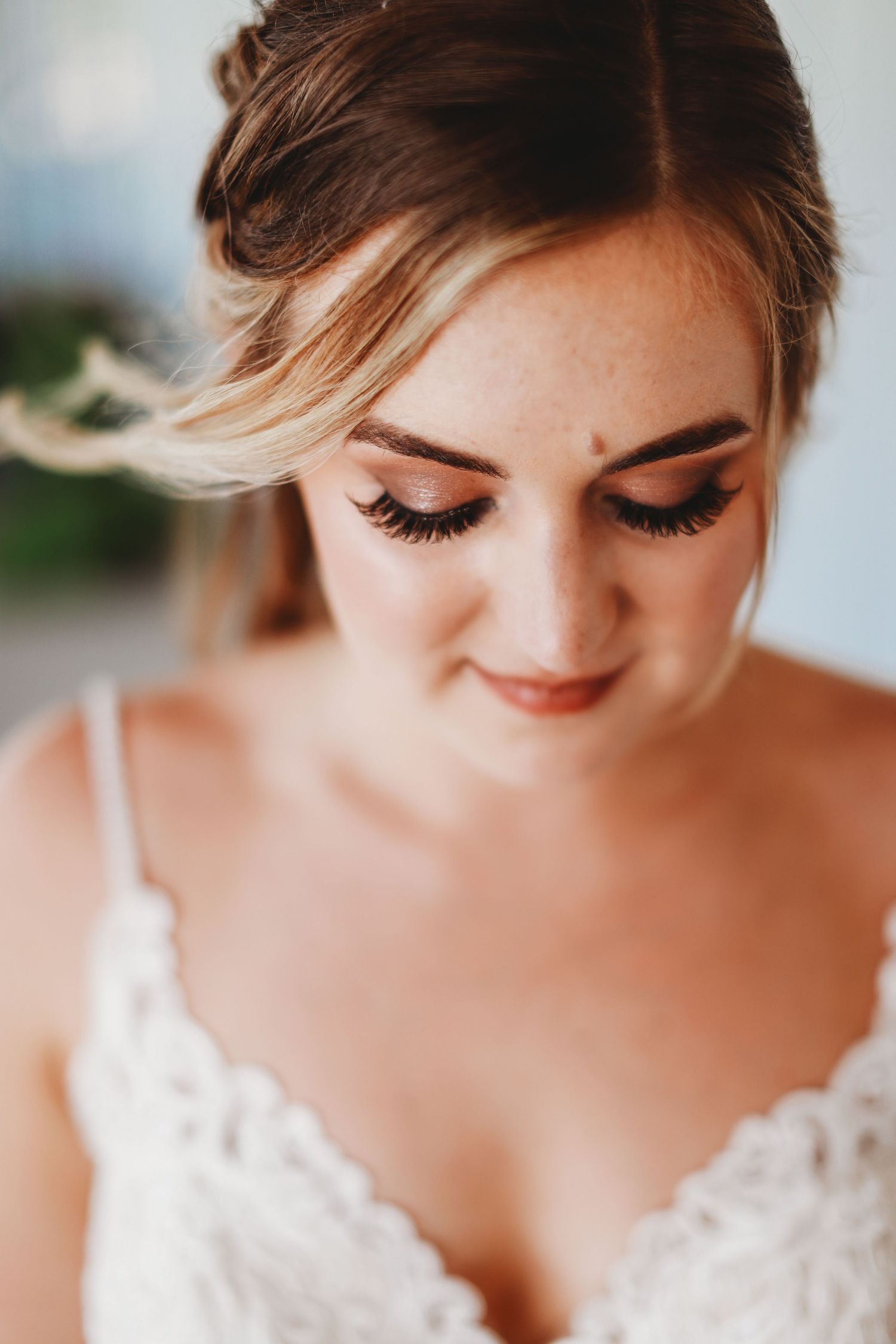 Close-up photo of a bride wearing a lace wedding dress and dramatic false eyelashes in soft natural lighting.