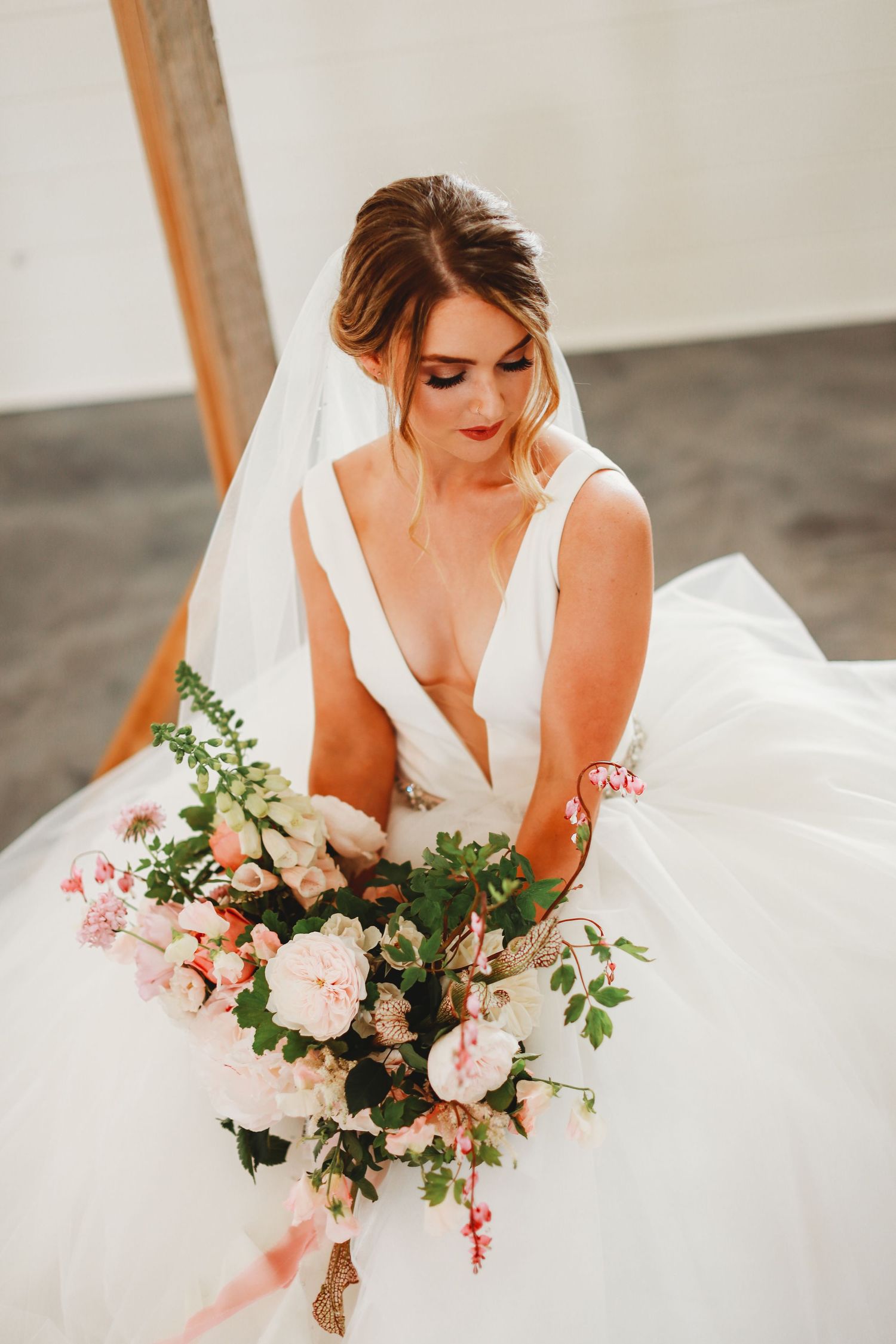 Bride seated in white gown holding beautiful pink and peach floral bouquet.