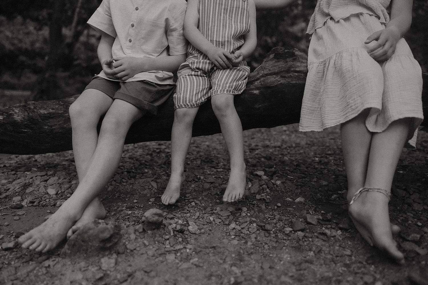 A black and white image of three children sitting on a log with their legs dangling down.