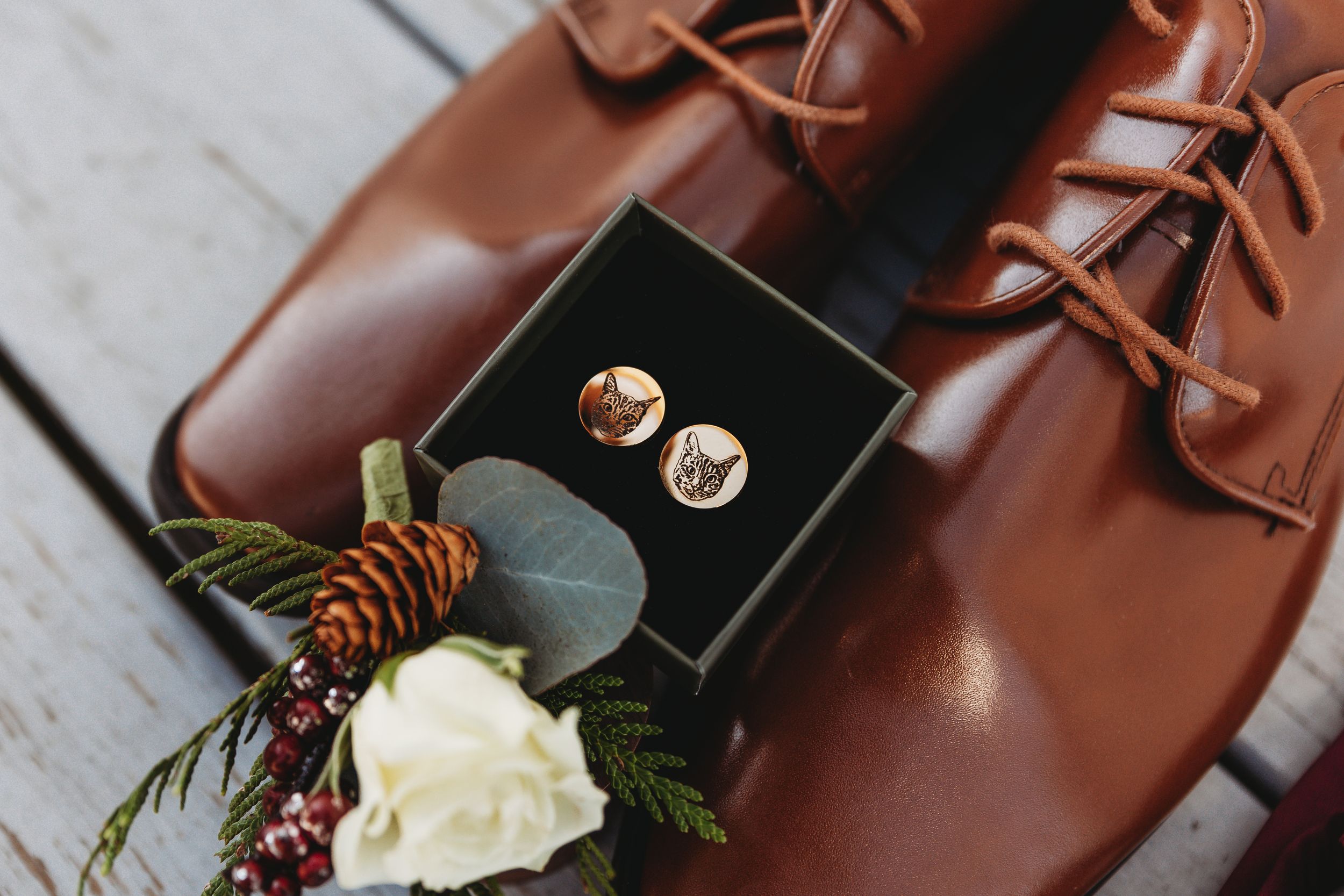 Brown leather dress shoes with wedding rings and white rose boutonniere.