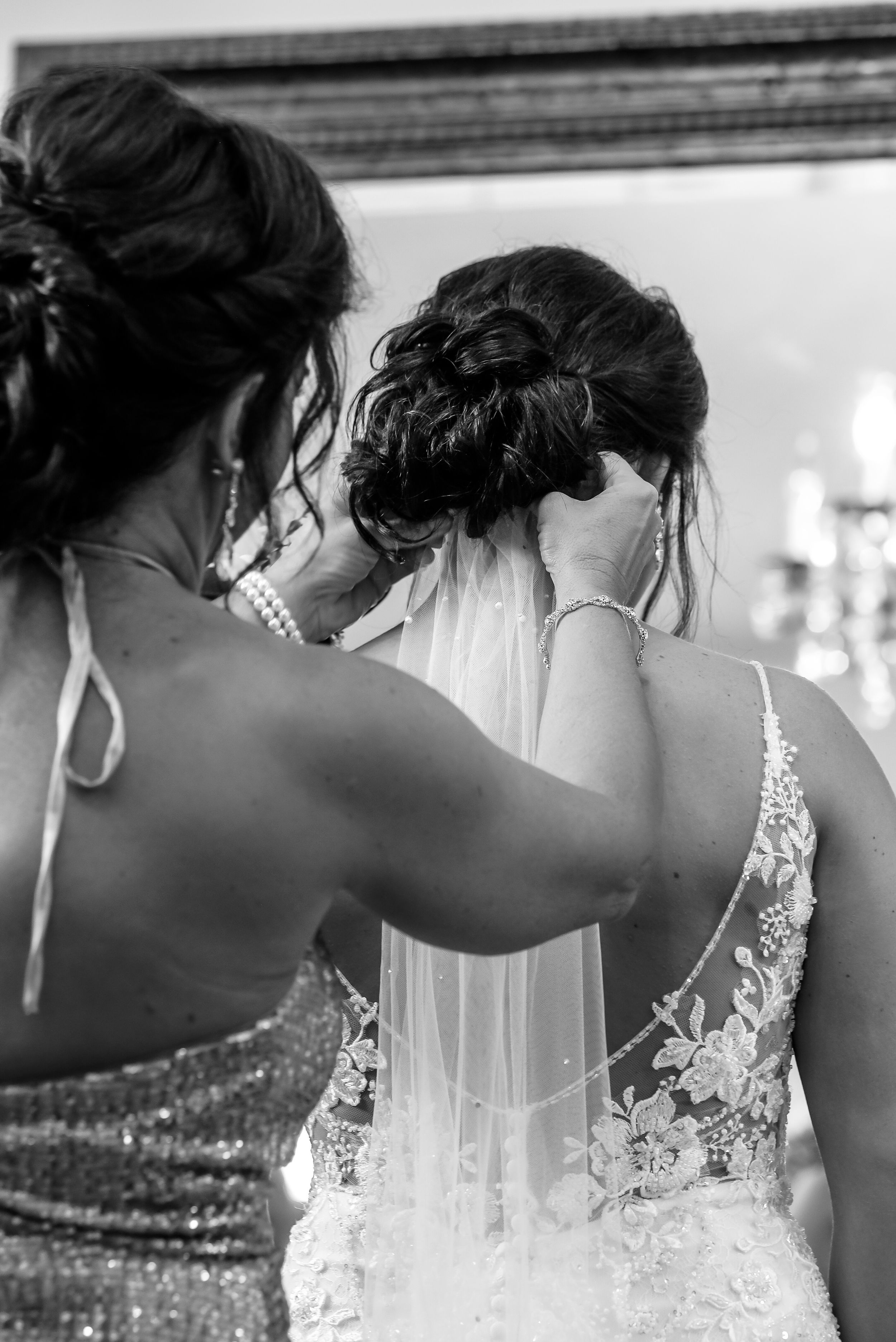 Black and white wedding photo showing final veil adjustments in an elegant mirror reflection.