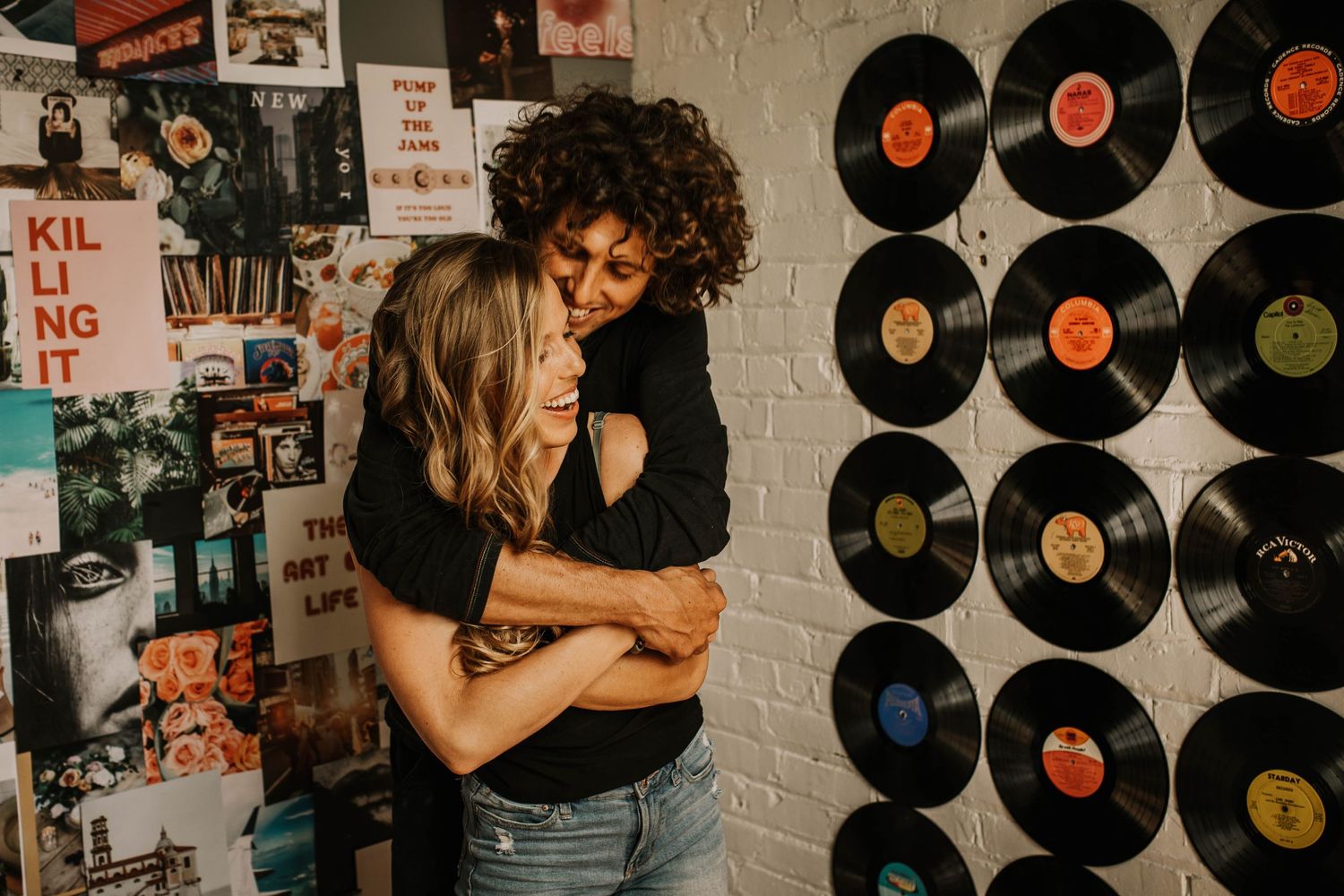 Two women joyfully hugging in front of a vinyl record wall and colorful poster display.