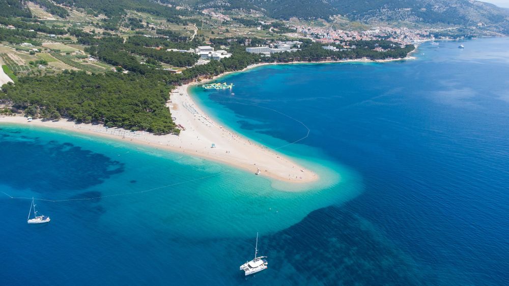 Aerial view of Golden Horn Beach jutting into turquoise waters with sailboats near Bol, Croatia.