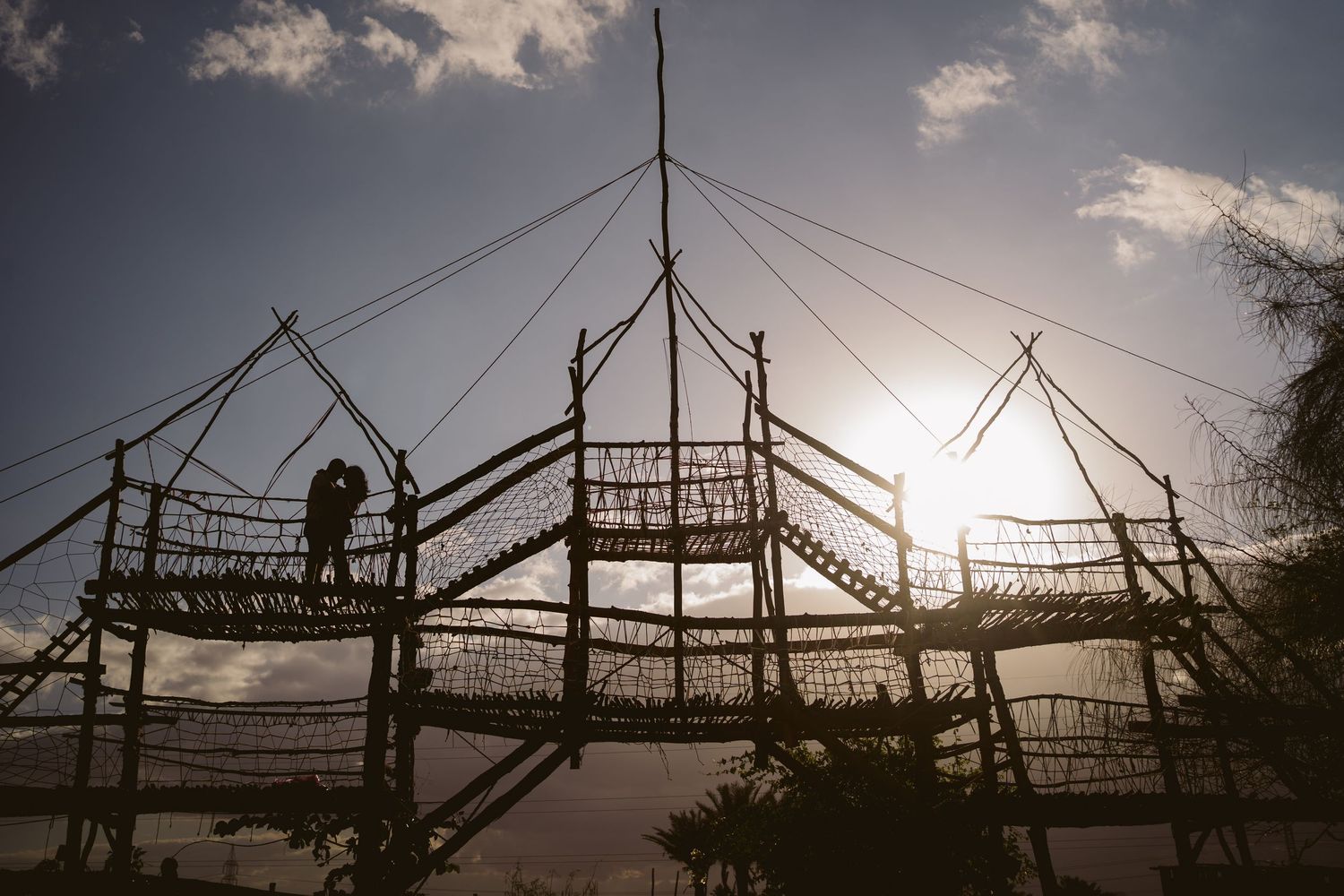 Silhouette of adventure rope bridge structure against dramatic sunset sky.