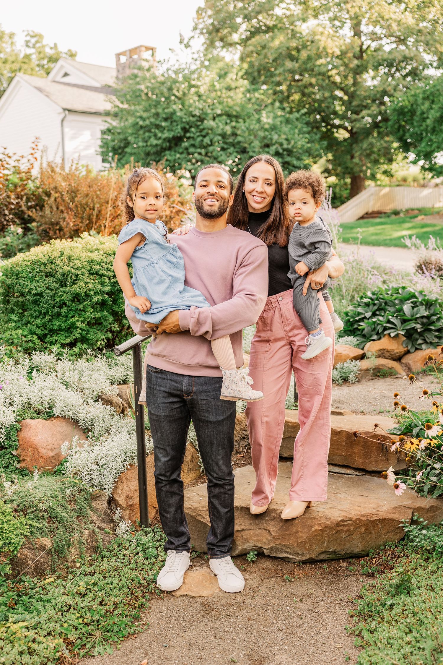 Family stands together on stone steps in a well-maintained garden landscape.