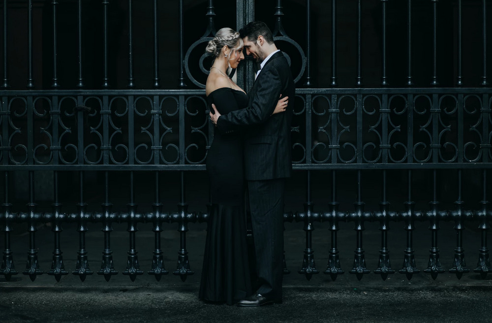 Silhouette of couple against ornate iron gate in dramatic black and white photo.
