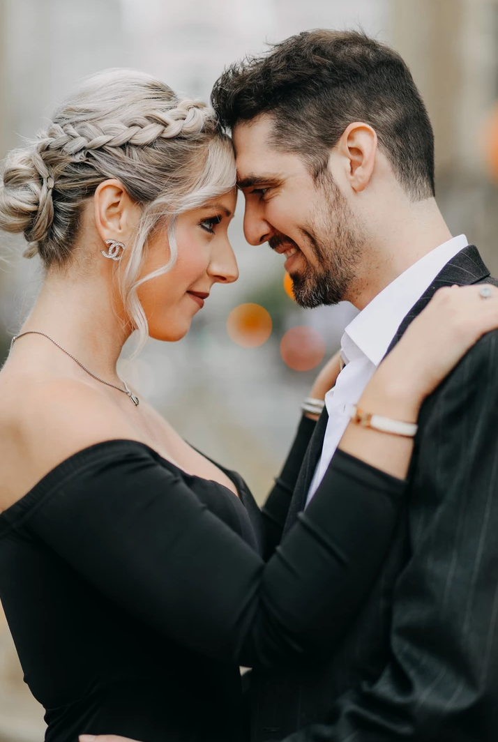 Elegant couple in formal wear share an intimate moment against blurred background.