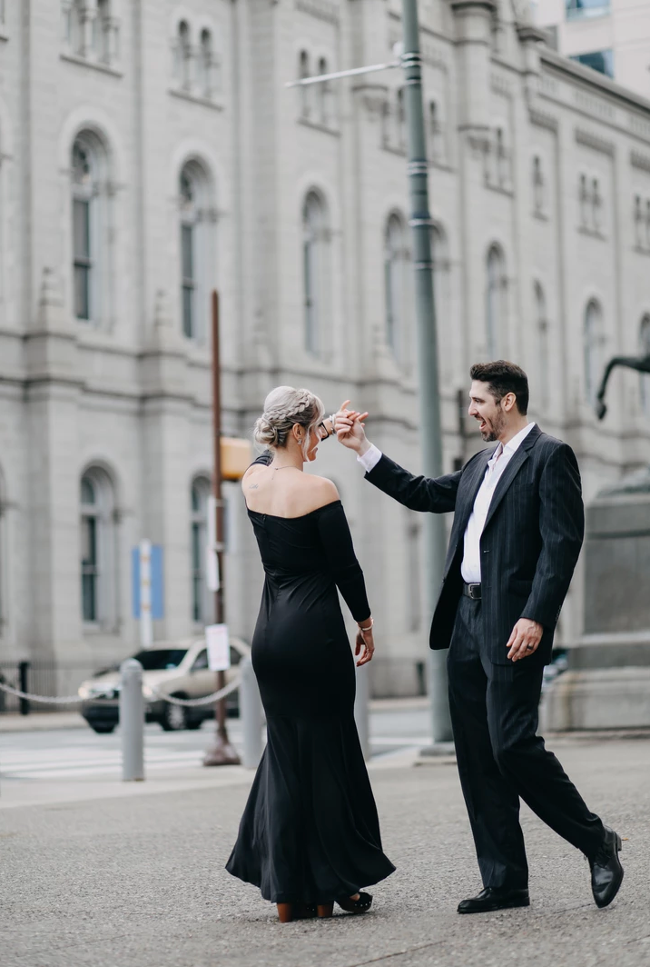Couple in formal attire dance in front of historic building.