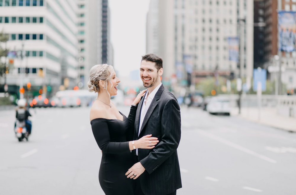 Happy couple in black formal wear embrace on urban street.