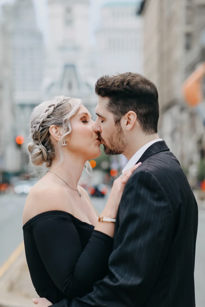 Romantic couple in formal wear share a kiss on city street.