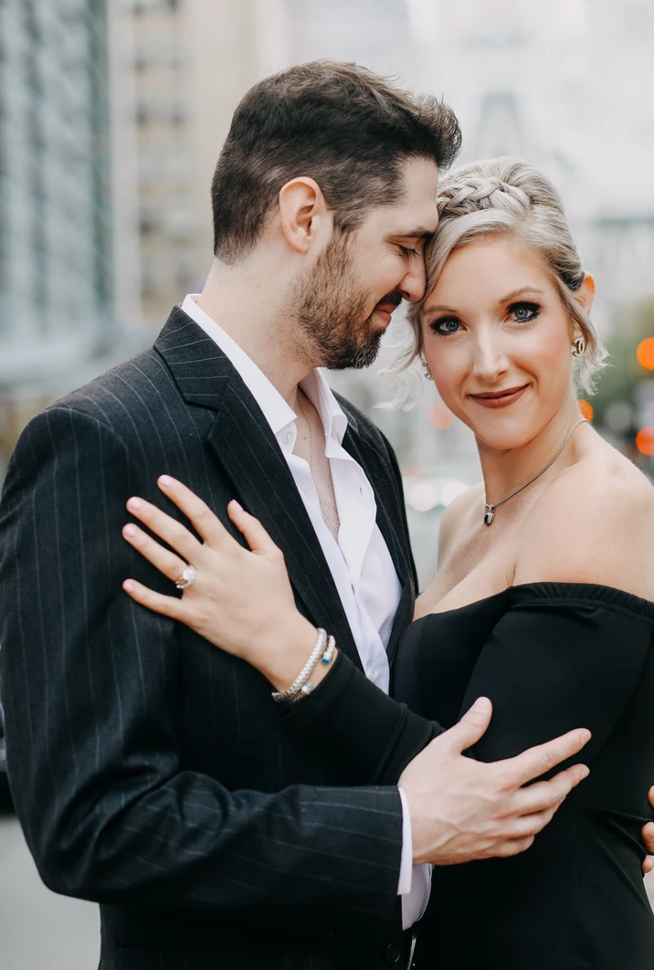 A romantic portrait of a couple in formal attire sharing an intimate moment against a city backdrop.