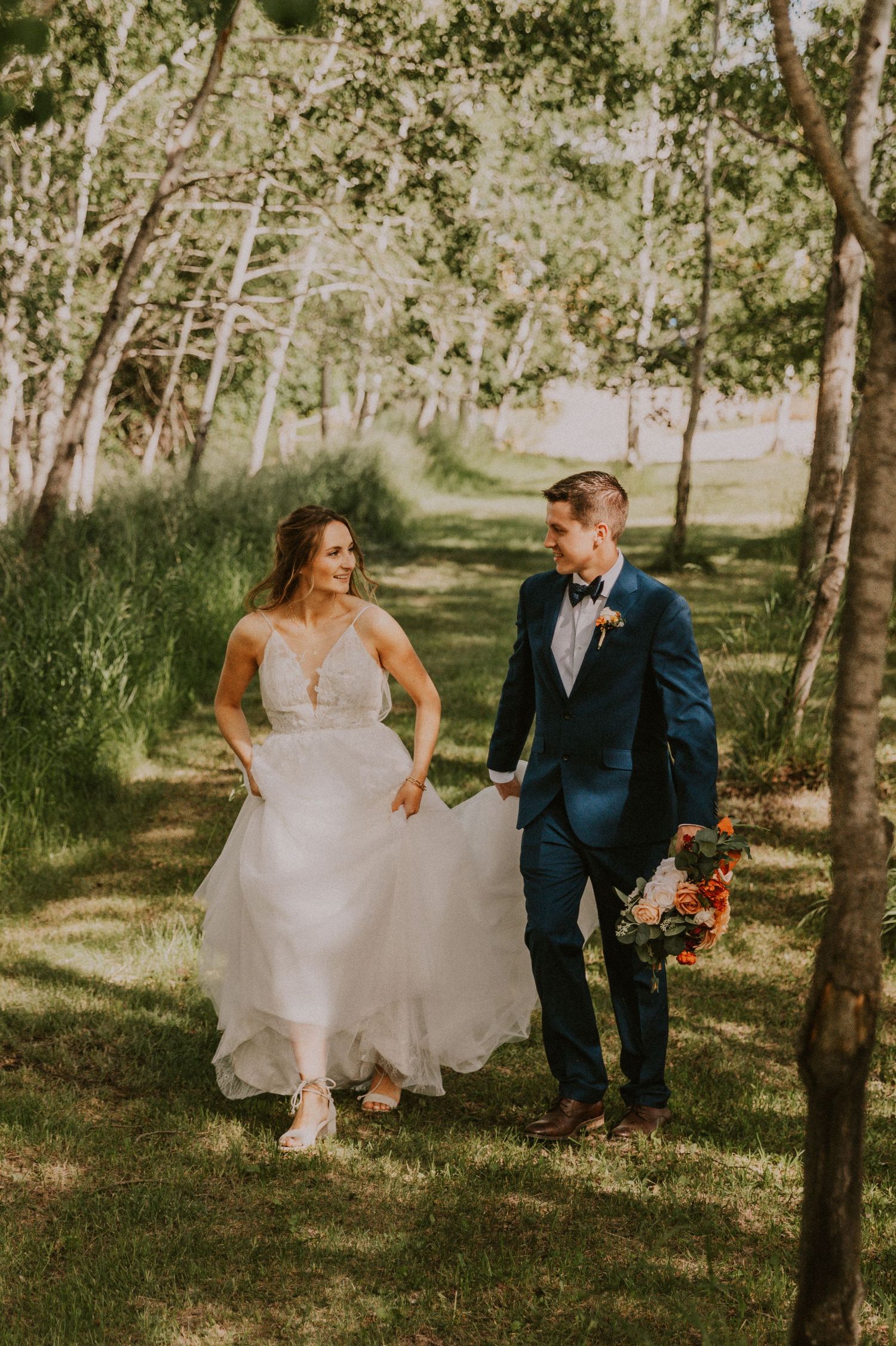 bride and groom walking through a field surrounded by trees
