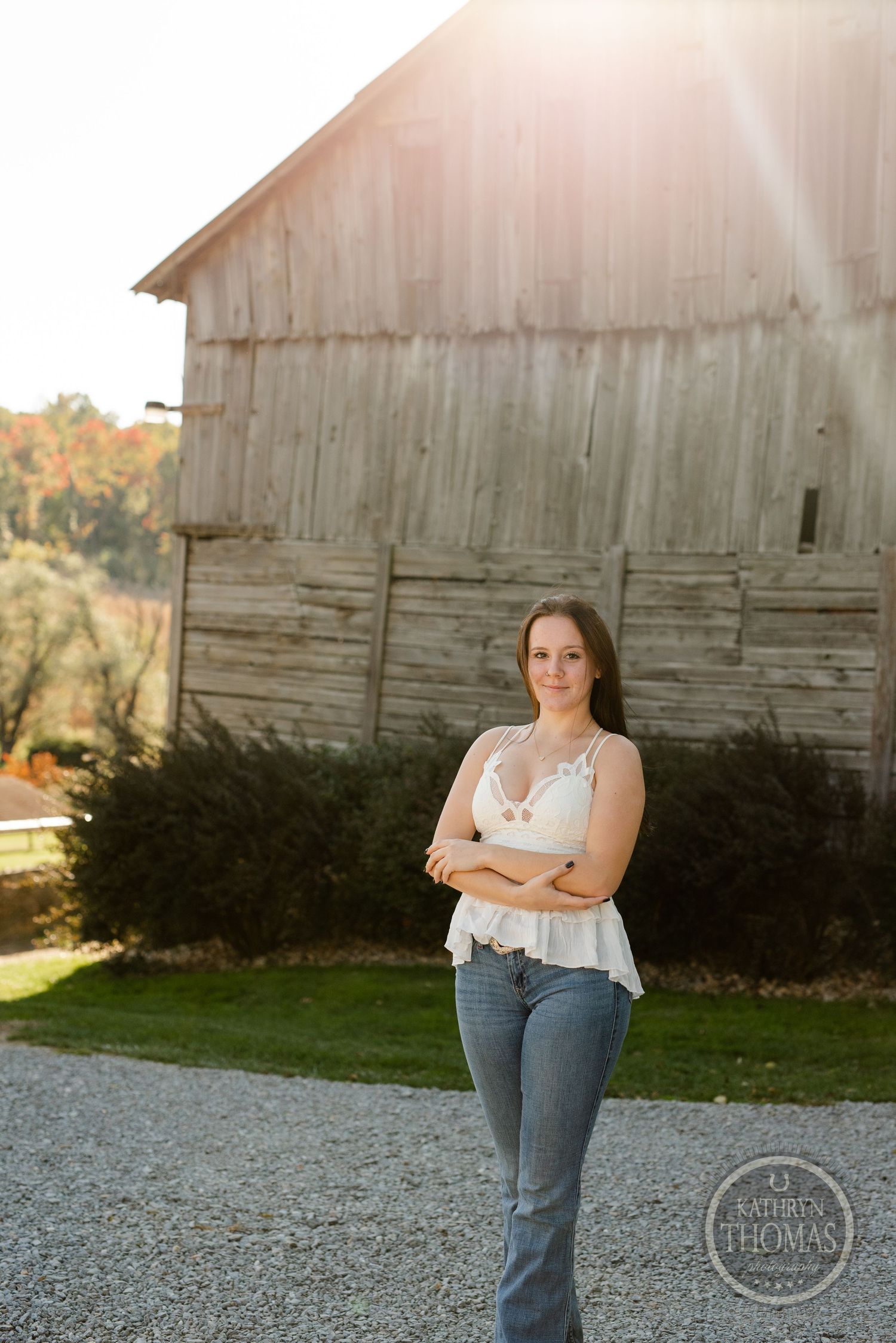 White lace top and jeans outfit posed in front of weathered barn at sunset.
