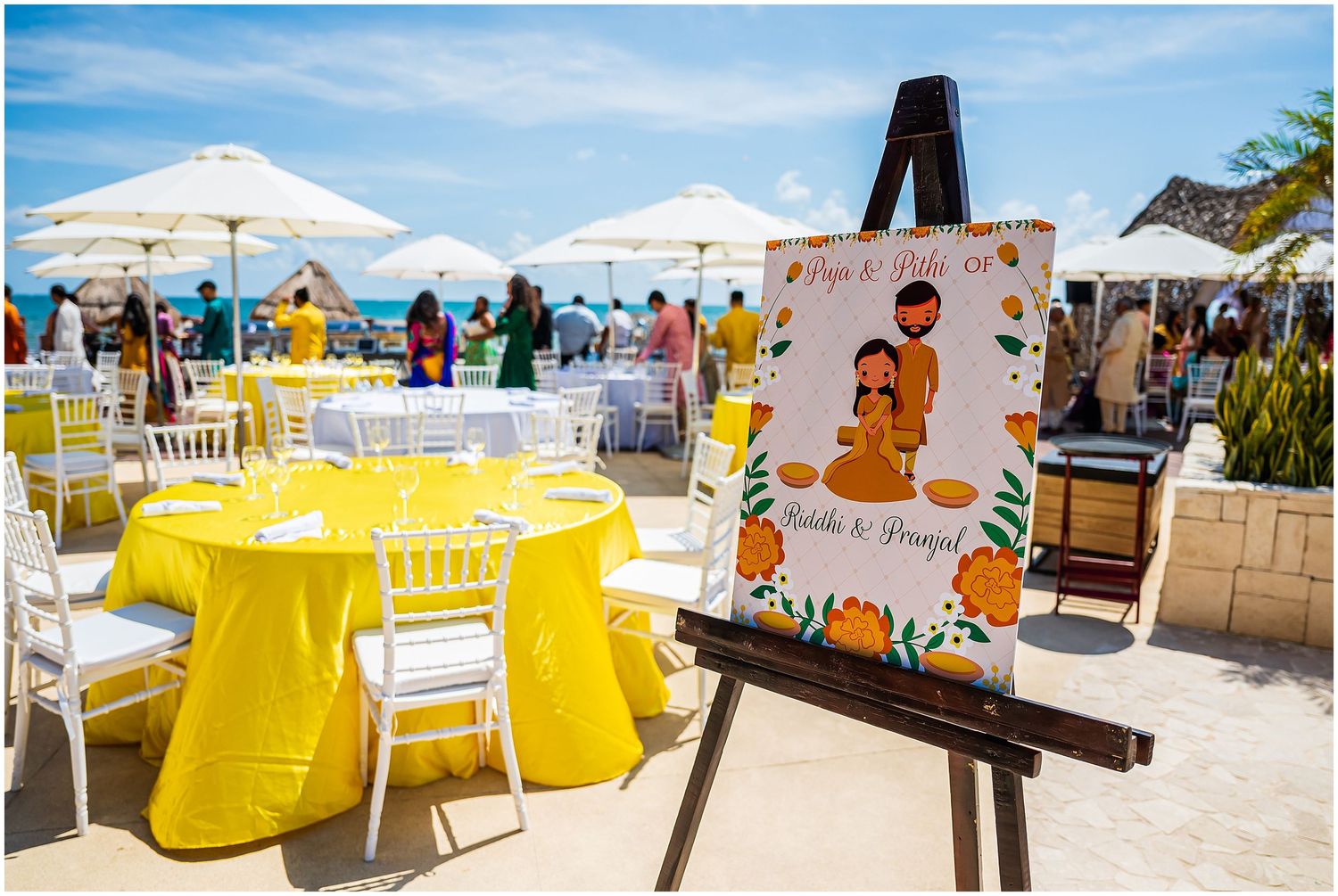 Outdoor beach wedding reception with yellow tablecloths and decorative welcome sign.