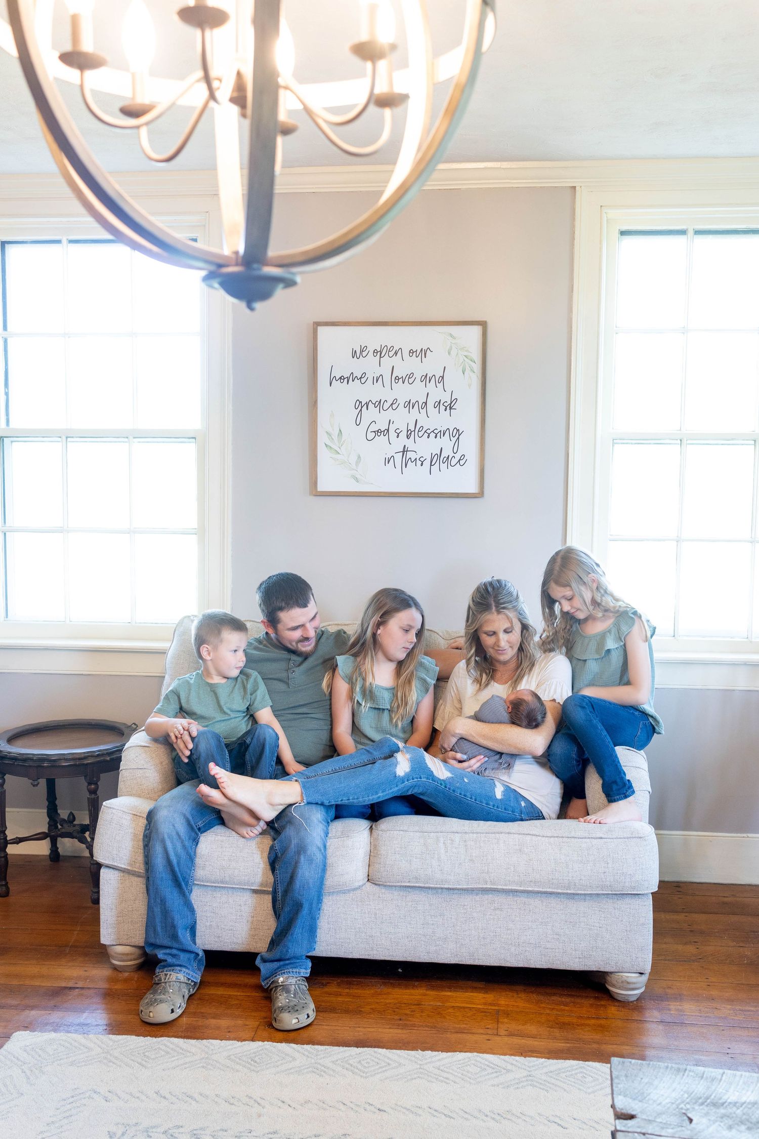 A casual family gathering on a gray couch under a modern chandelier in a bright living room.