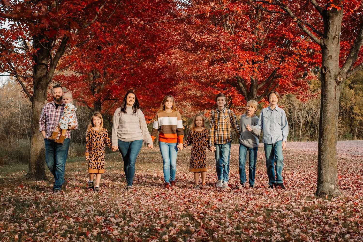 A group walks together under vibrant red fall foliage trees.
