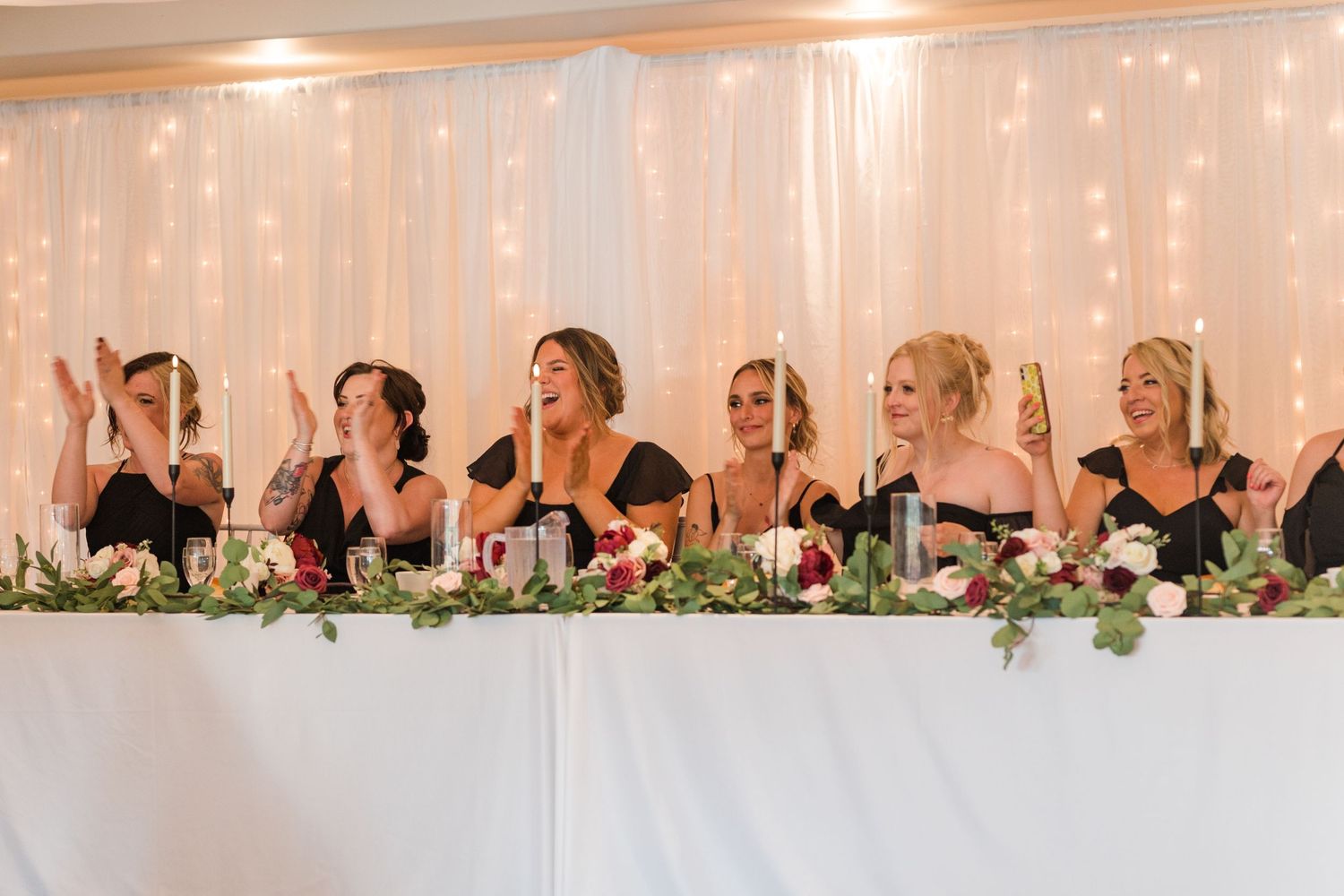 Long wedding reception head table decorated with greenery and string lights creating a romantic atmosphere.