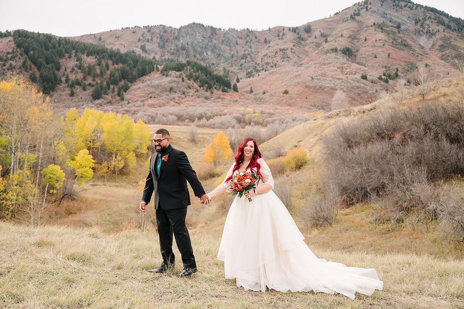 A couple shares a joyful moment on their wedding day surrounded by fall mountain scenery.