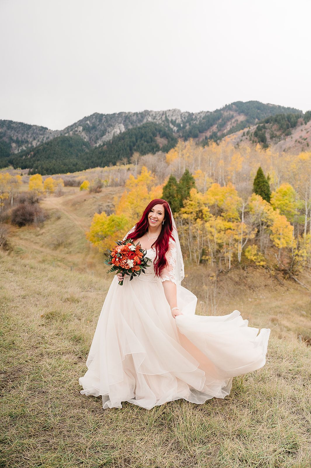 A bride's dress flows in the wind against yellow aspen trees and mountain landscape.