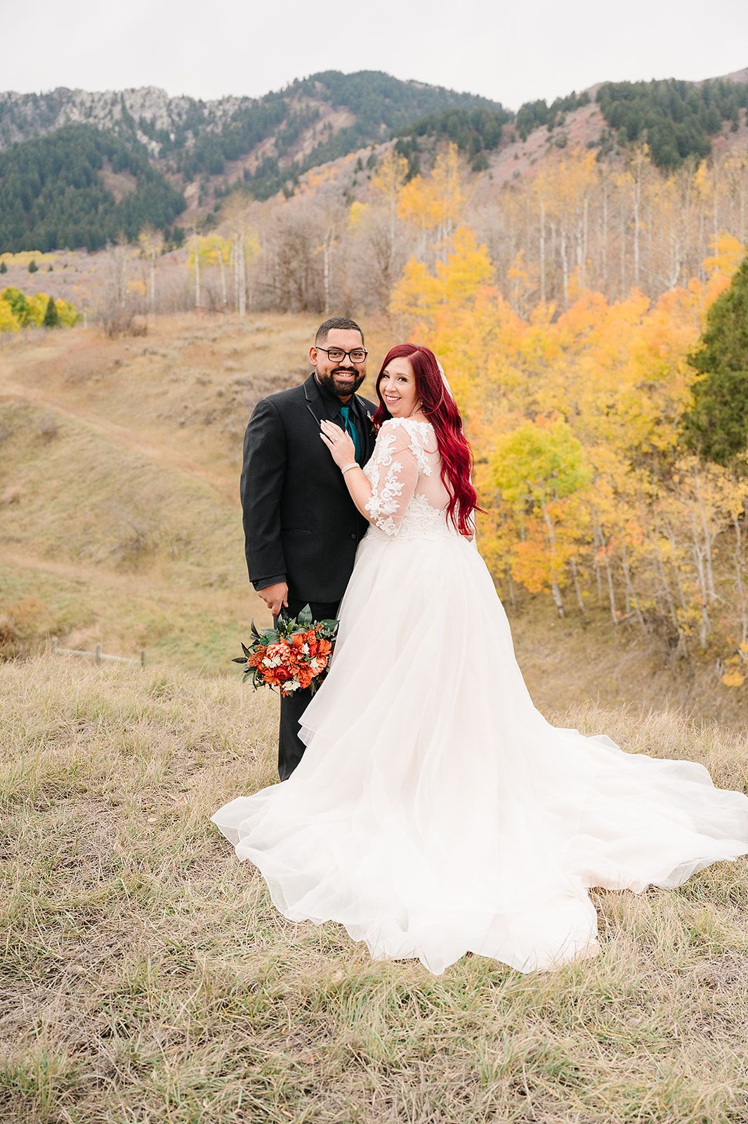A wedding couple embraces against a backdrop of golden fall foliage in the mountains.