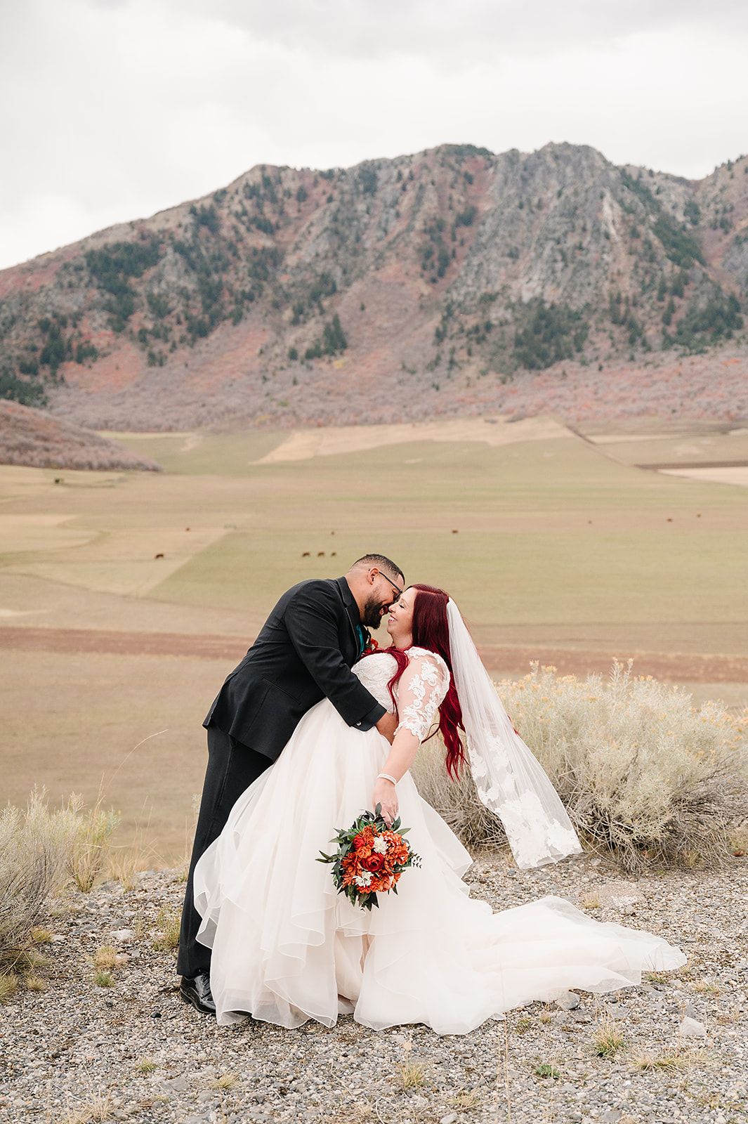 A romantic wedding photo in front of rugged mountains with a beautiful autumn-colored bouquet of flowers.
