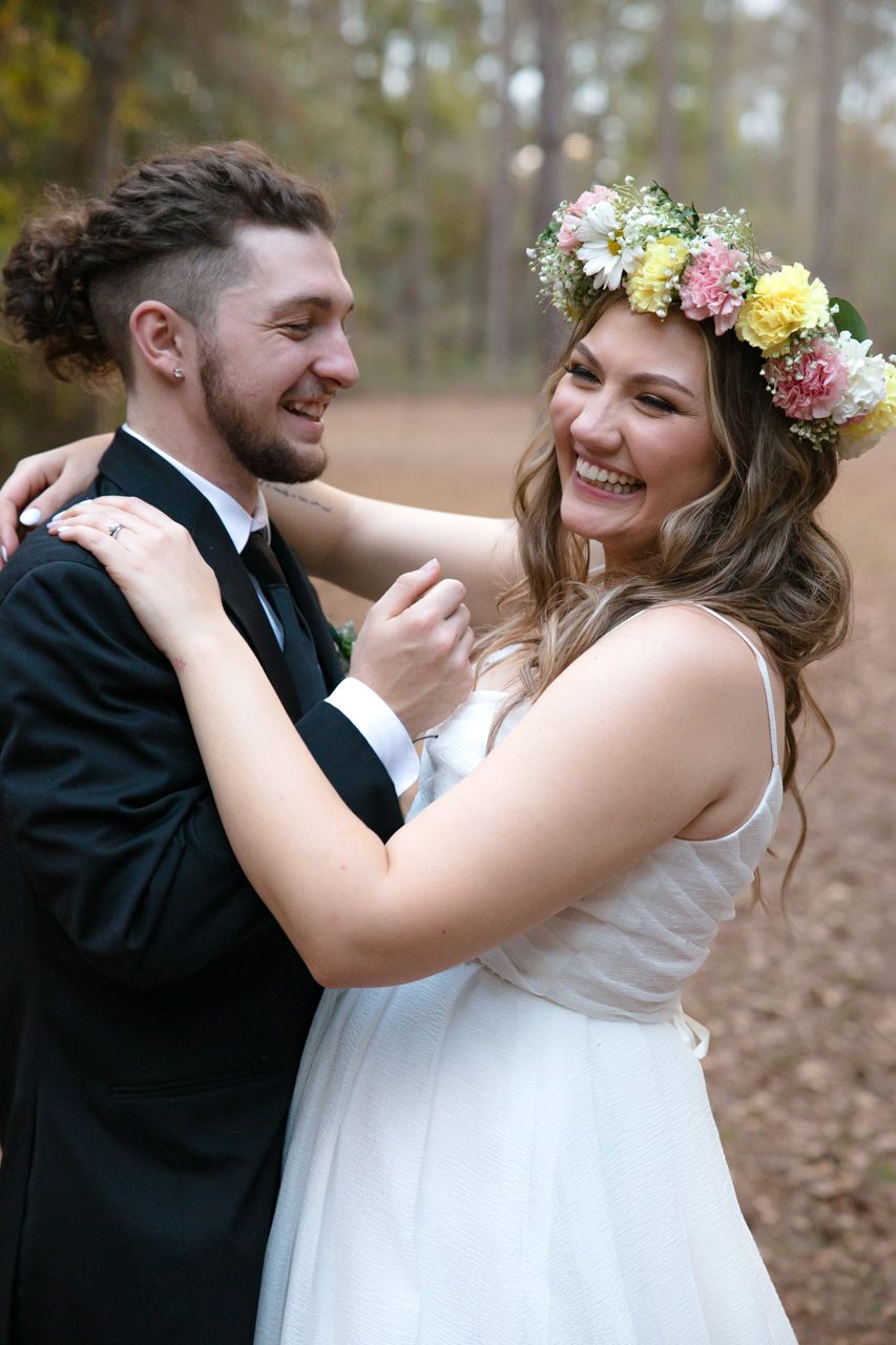Bride with flower crown and groom share intimate moments during woodland wedding photos.