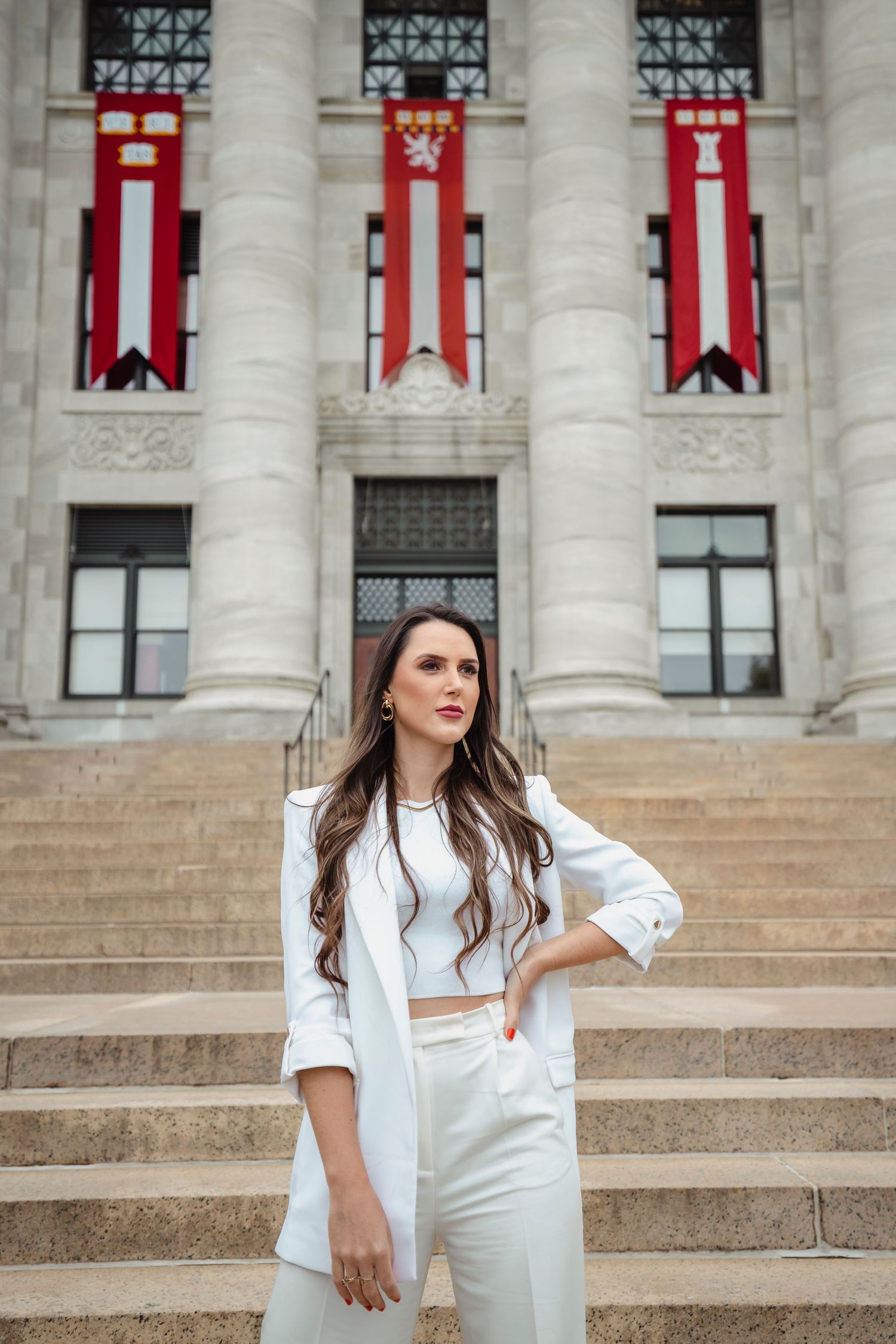 Professional fashion photo series of someone in white attire posing on grand marble building steps with red banners.