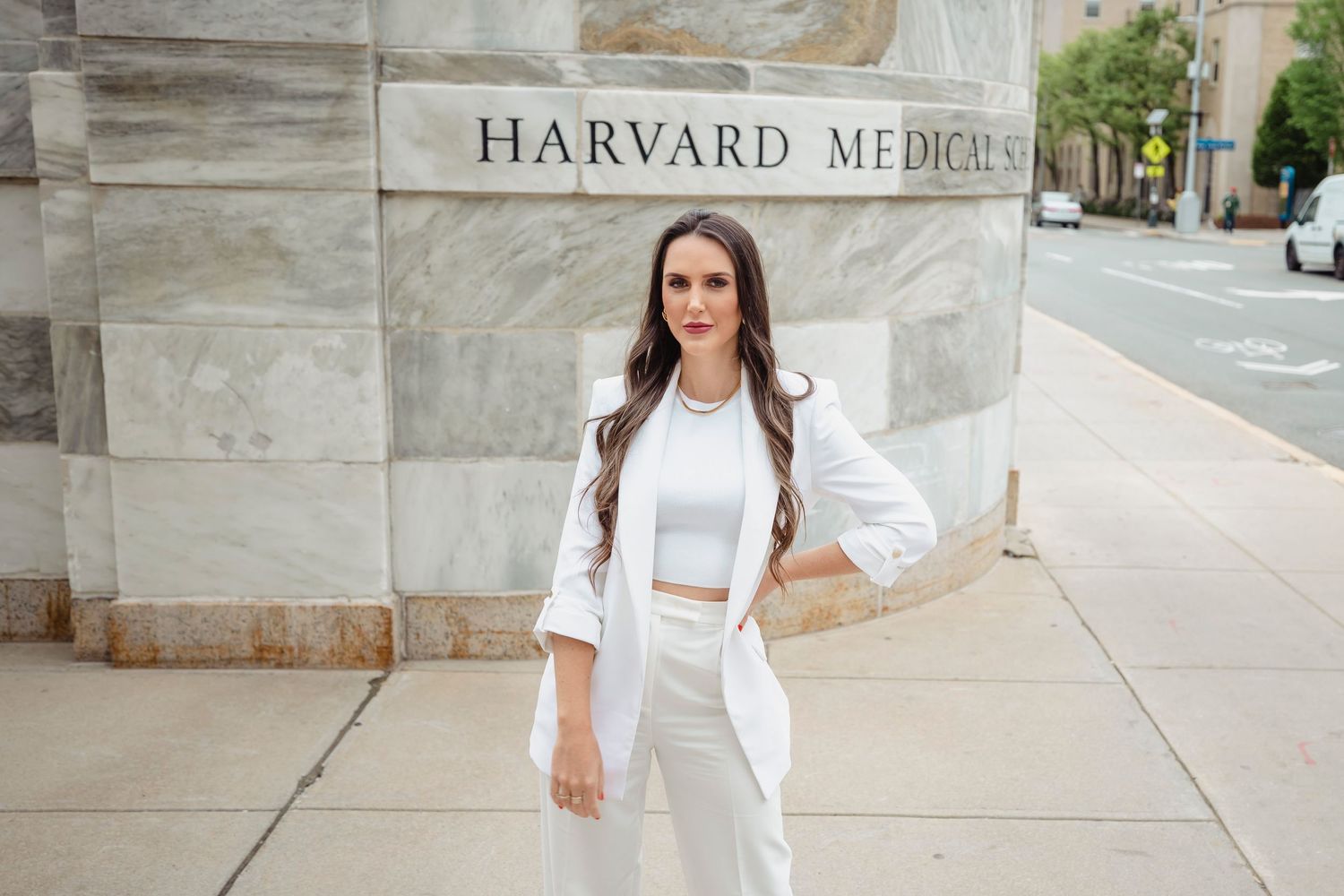 A healthcare professional in an all-white outfit stands confidently outside Harvard Medical building entrance.