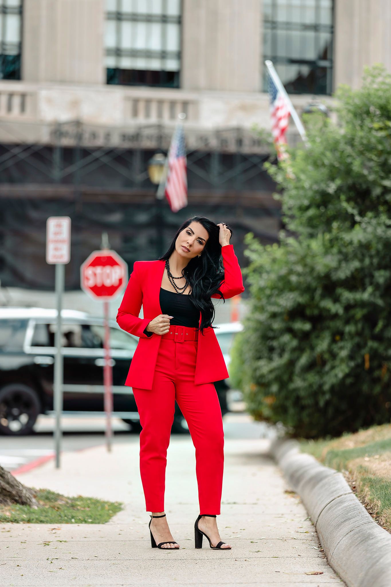Fashion photoshoot outdoors featuring model in vibrant red pantsuit posing on urban sidewalk.