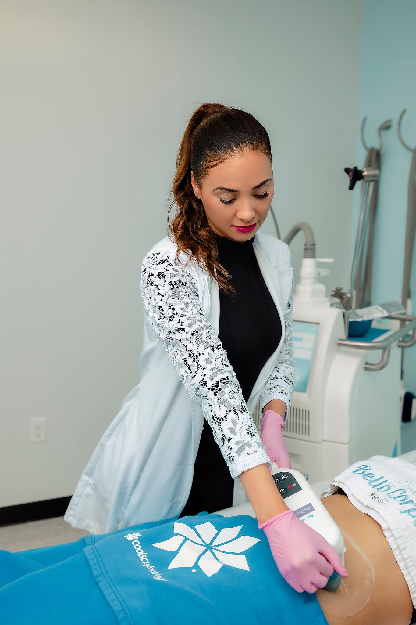 Technician performing cosmetic treatment wearing white lace sleeve uniform and pink gloves.