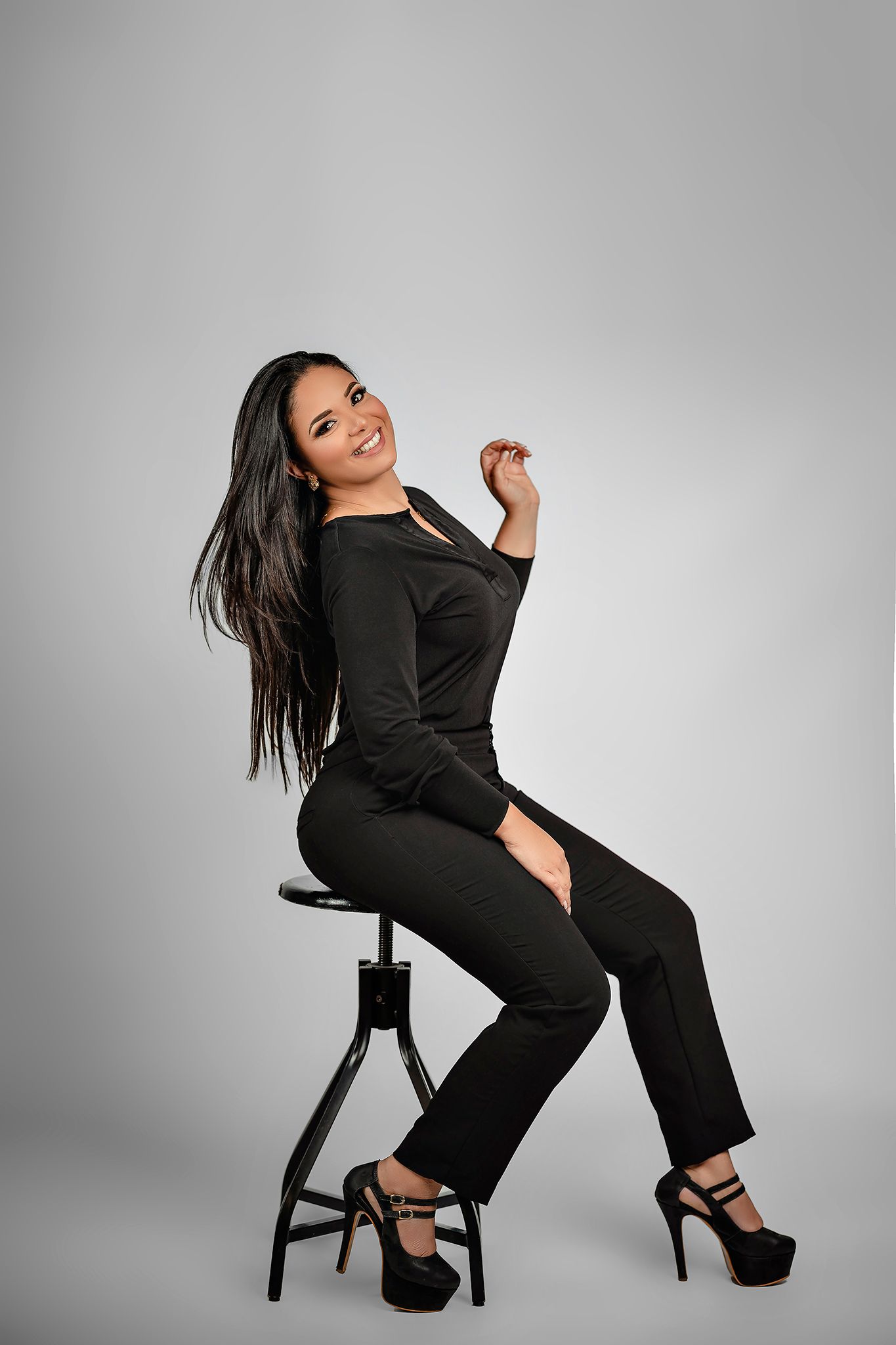 Dynamic pose in black ensemble on studio stool with platform heels.
