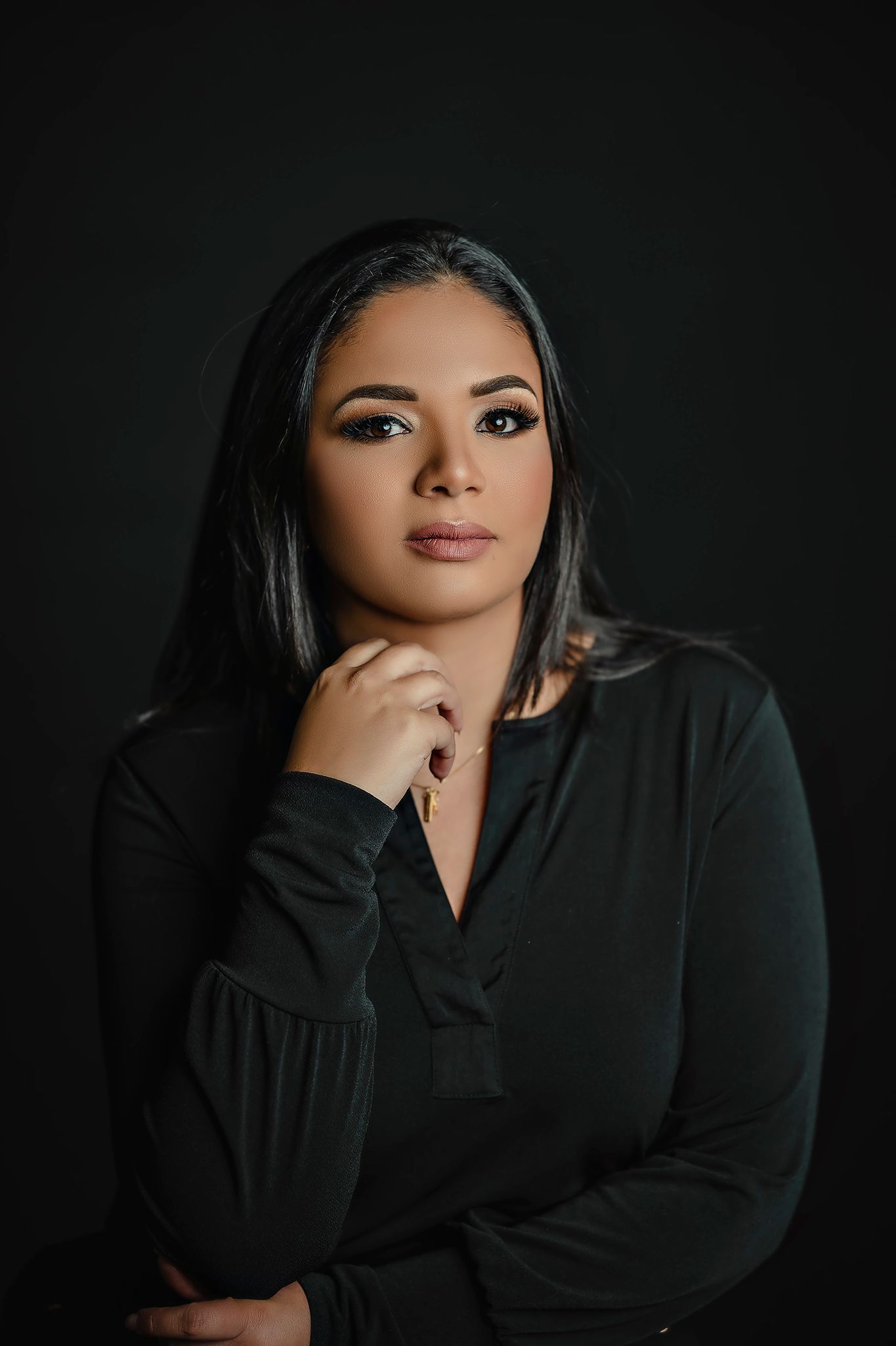 Professional studio portrait featuring dark sophisticated makeup and black attire against a moody dark background.