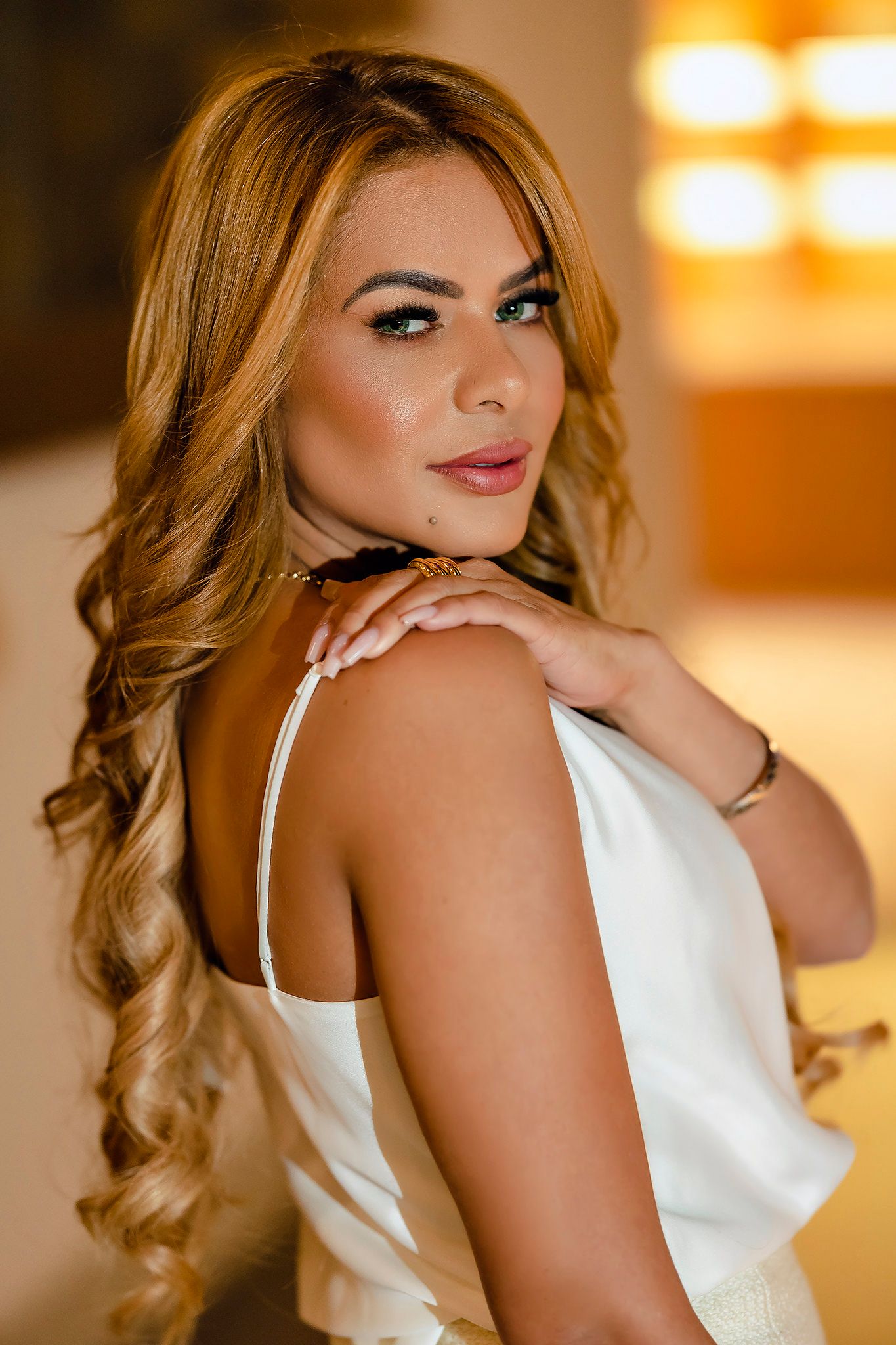 Portrait of woman in white top with styled wavy hair against warm background.