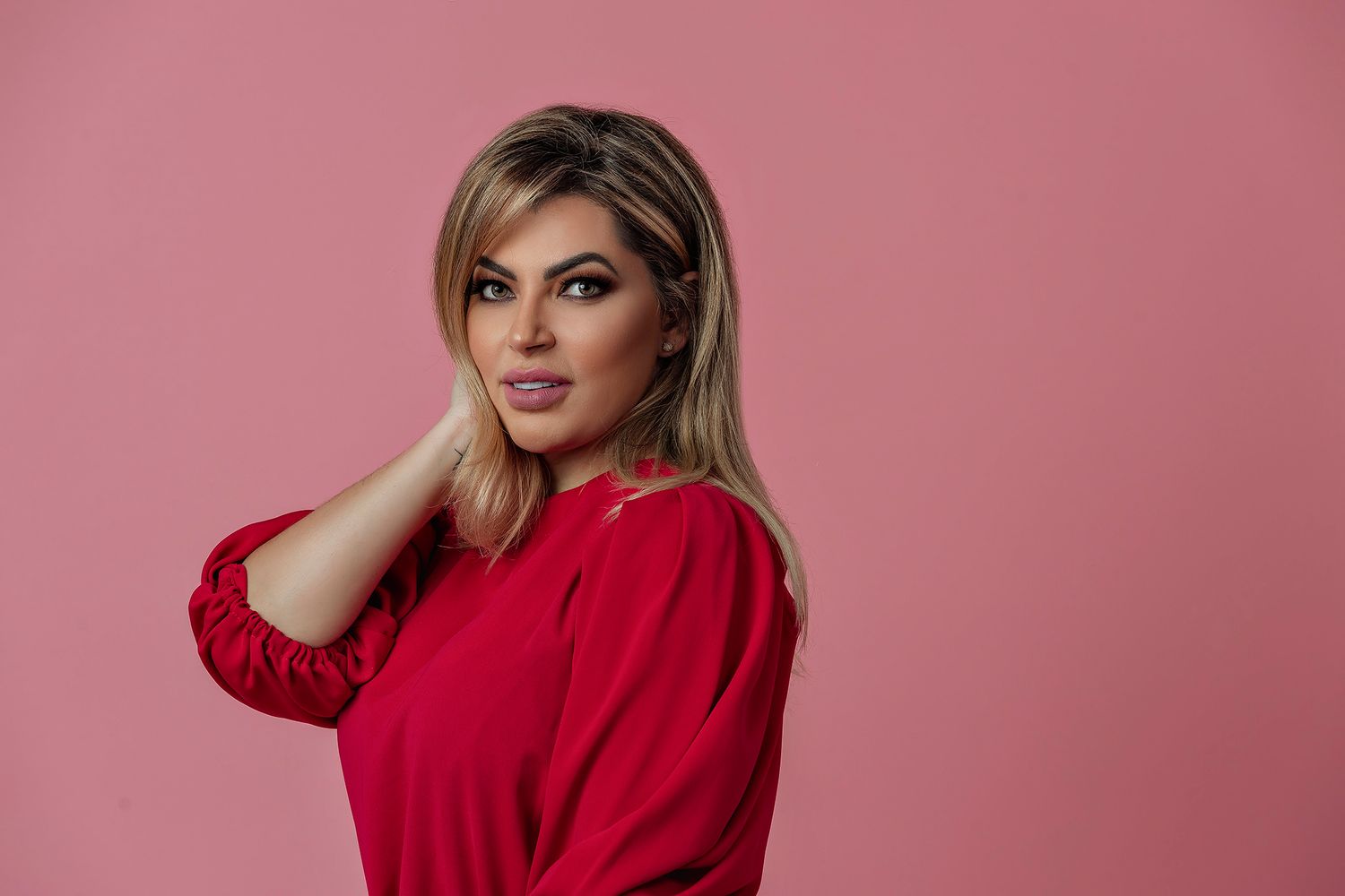 Studio portrait featuring a red sweater against a pink backdrop.