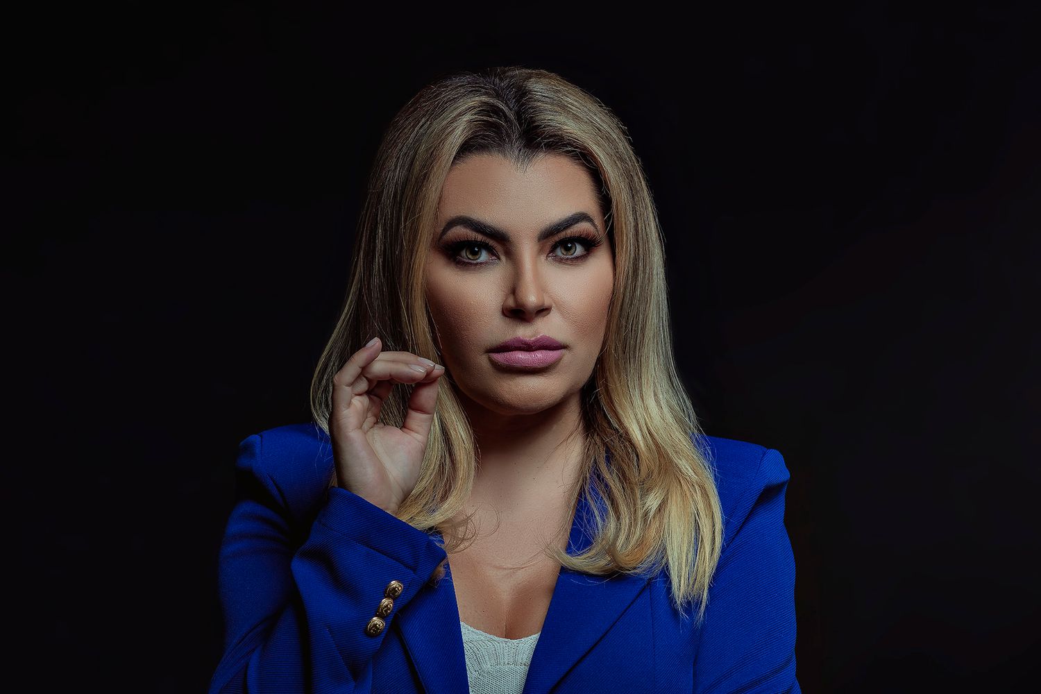 Dramatic portrait in a royal blue blazer against a dark background.
