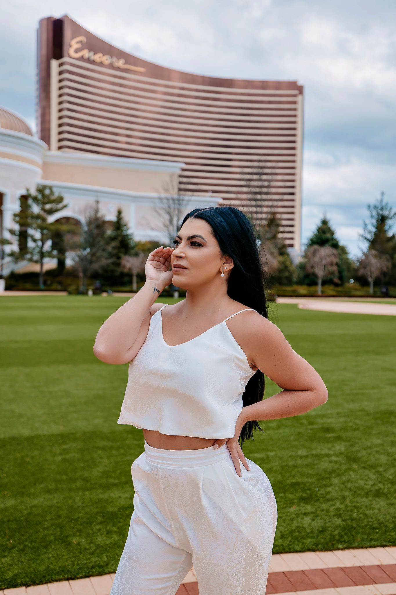 Female model in white activewear poses outdoors with luxury resort building in background.