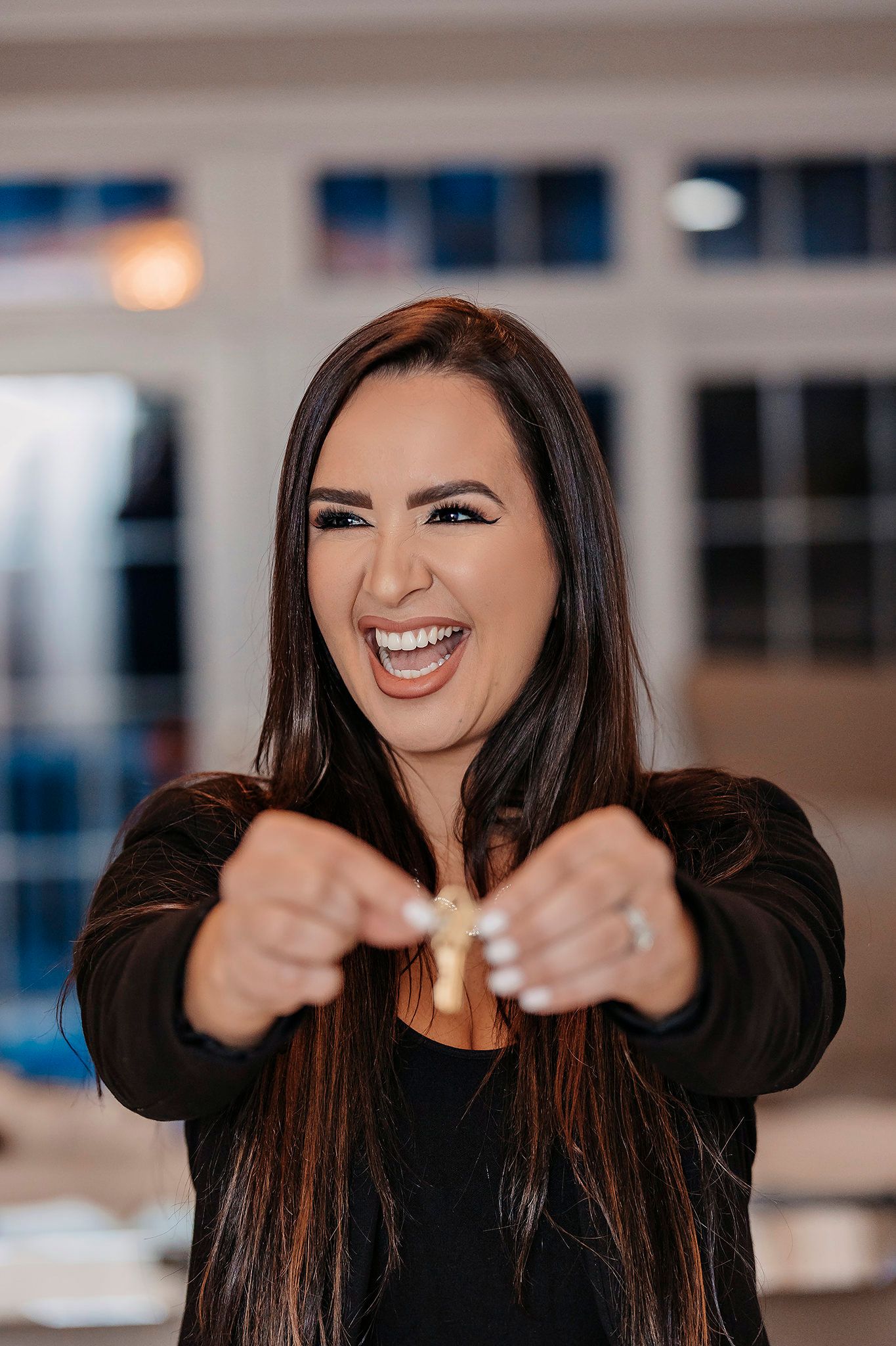 Portrait of woman with long dark hair laughing and pointing with enthusiasm.
