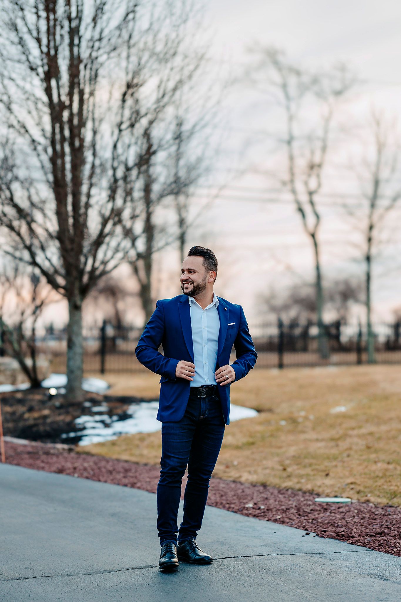 Man in blue suit walks confidently on outdoor path with landscaped grounds in background.