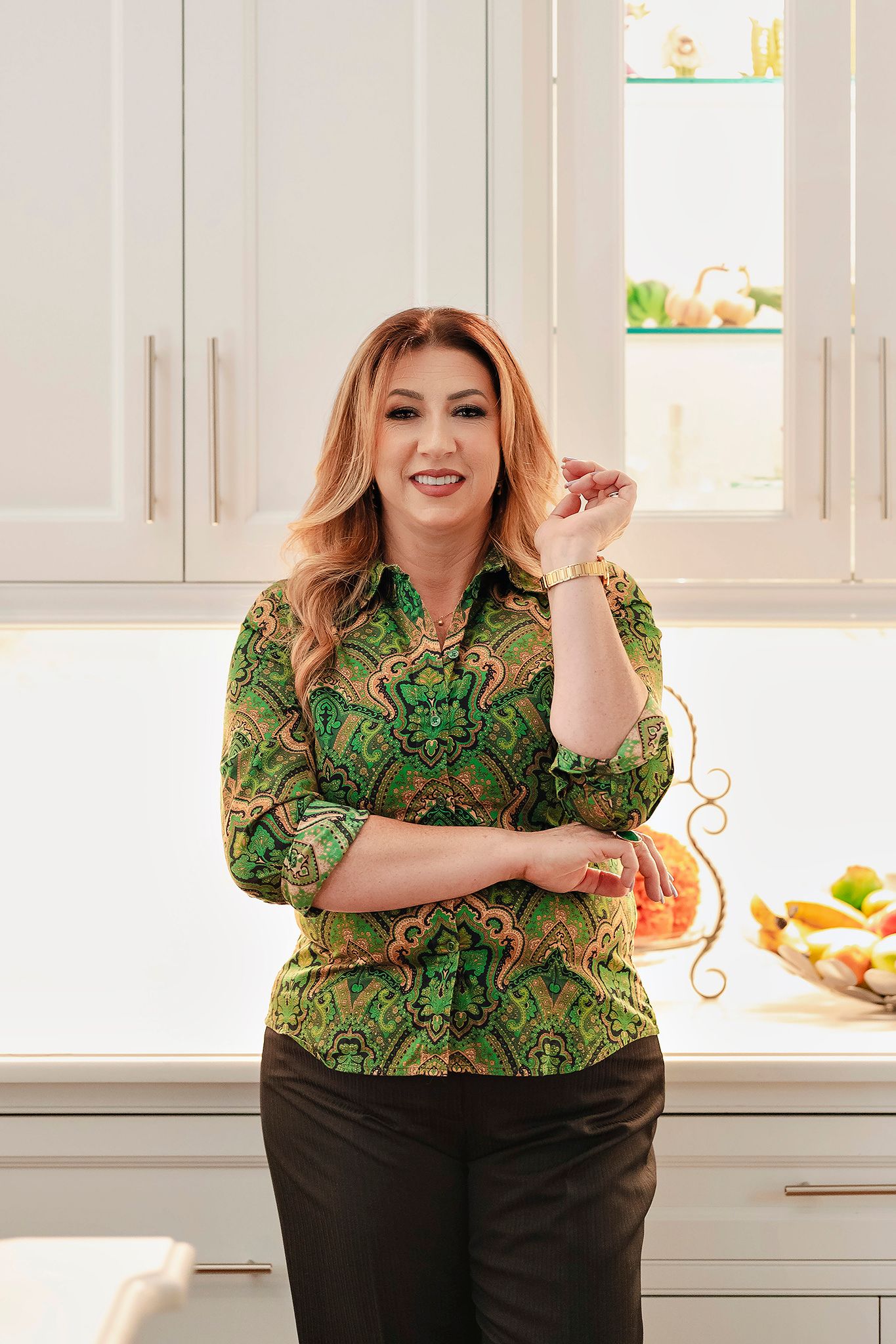 A person in a green patterned top poses against white kitchen cabinets.