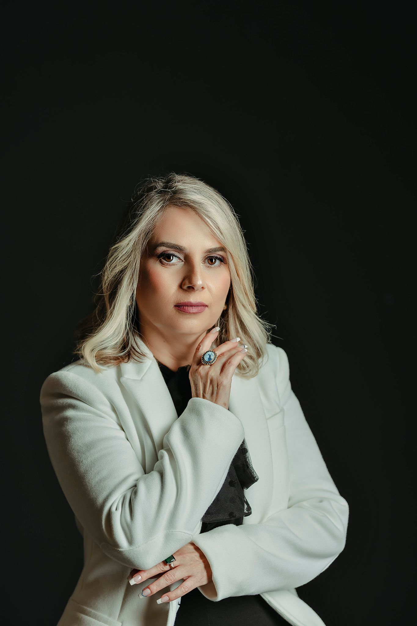 A portrait against black background wearing a white oversized blazer with dramatic lighting.