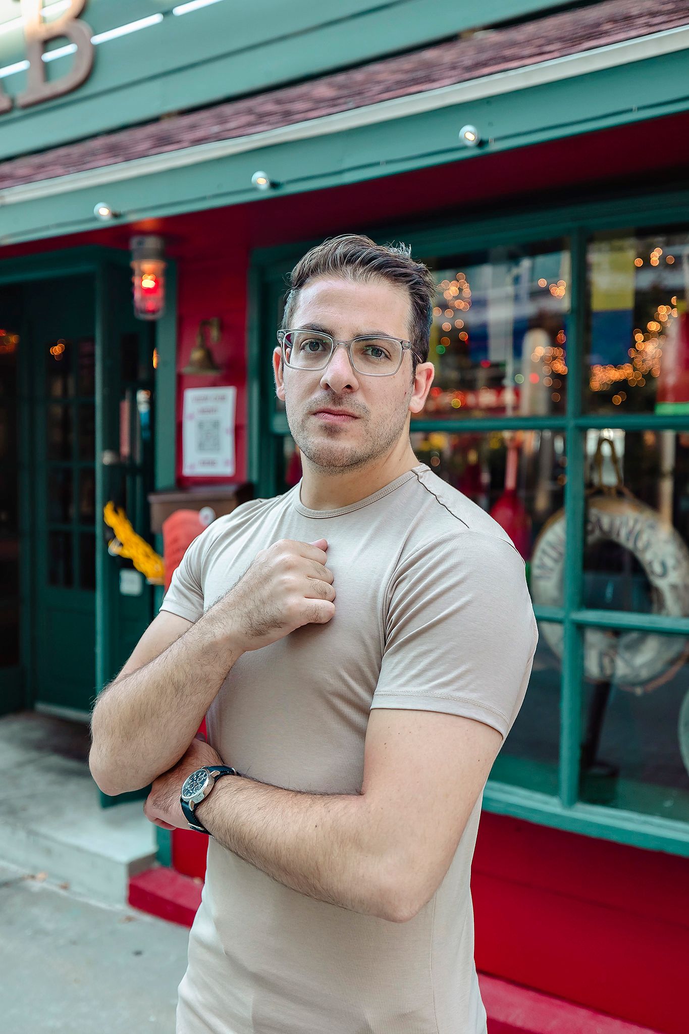 Person in fitted beige t-shirt poses confidently outside storefront with green awning.