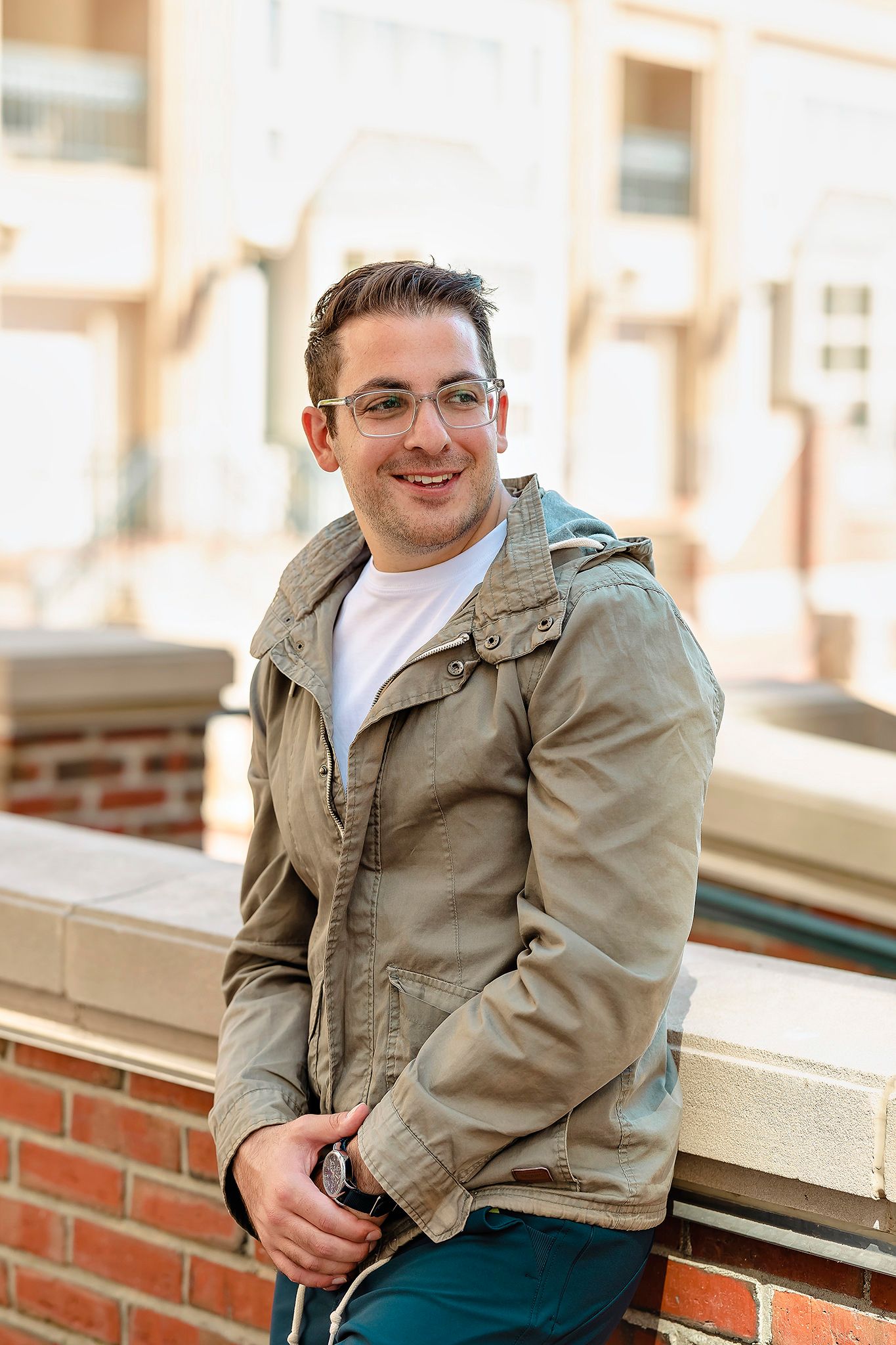 Casual outdoor portrait of person wearing tan jacket and glasses against brick building.