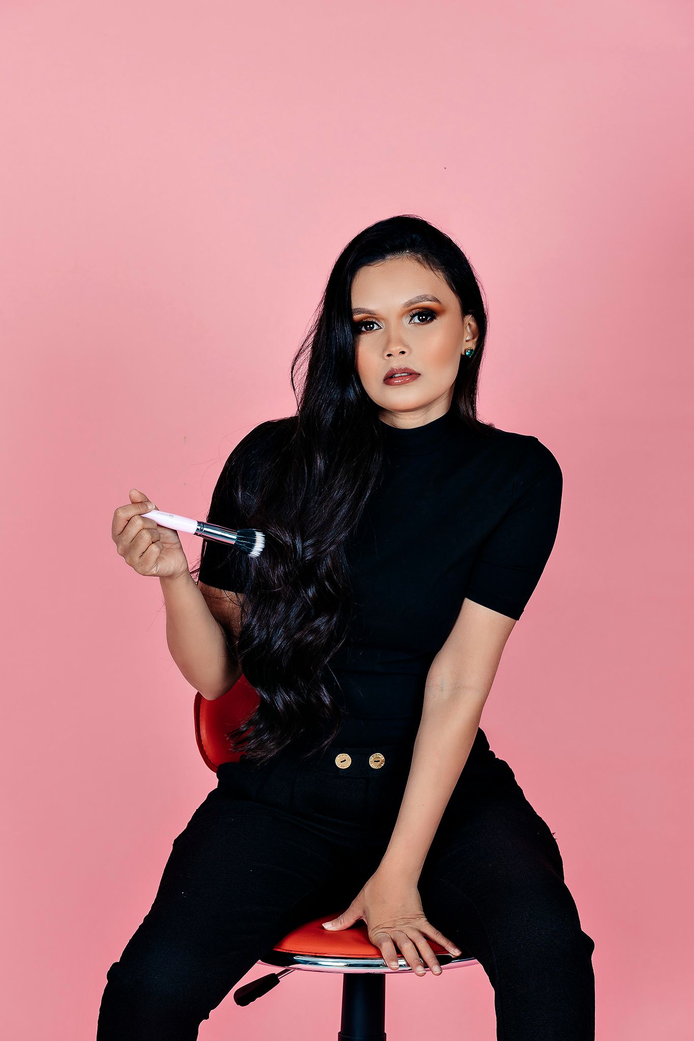 Modern fashion pose in black outfit on a bright pink studio backdrop.