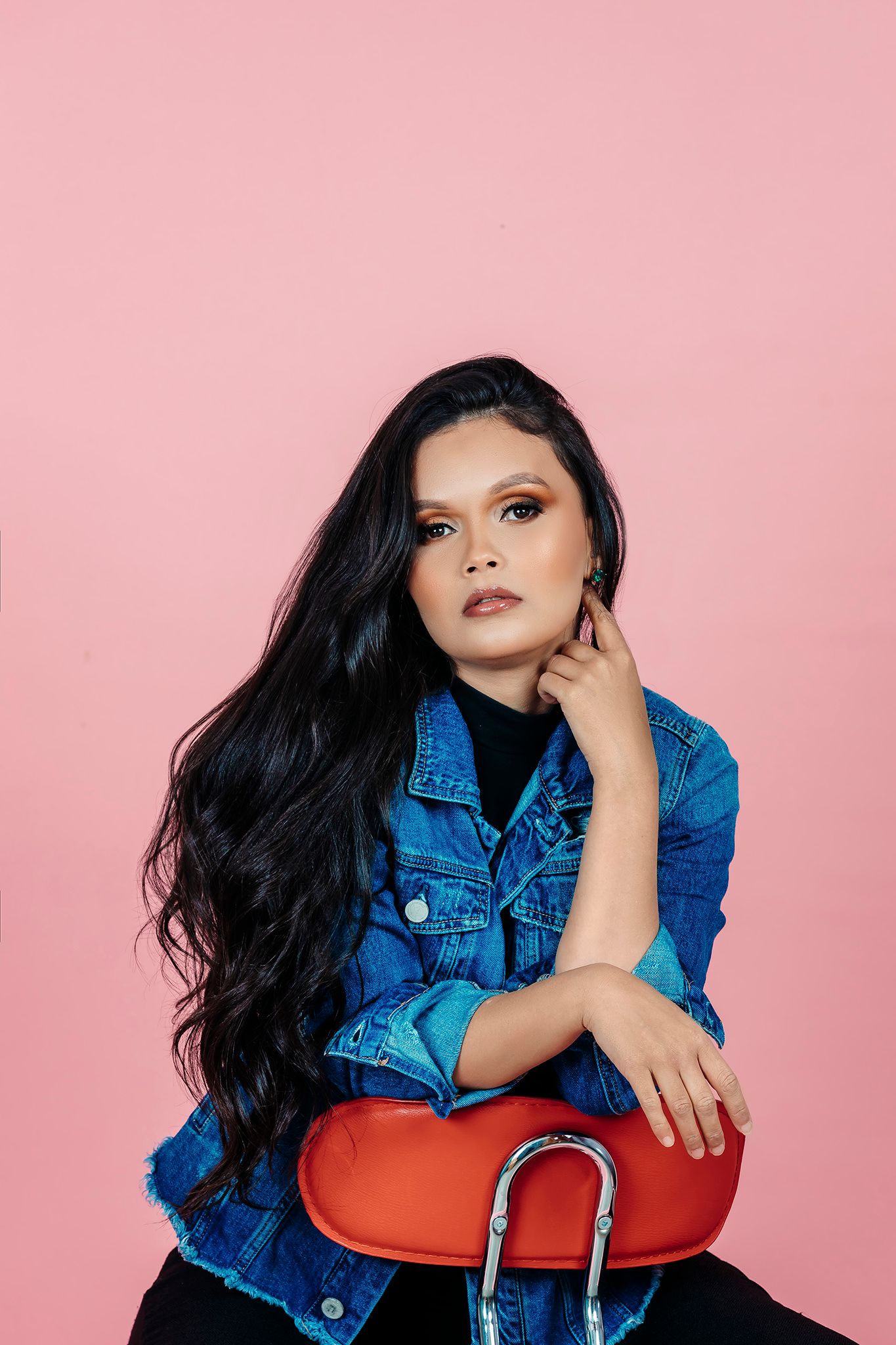 Stylish denim jacket look photographed against vibrant pink background with dramatic pose.