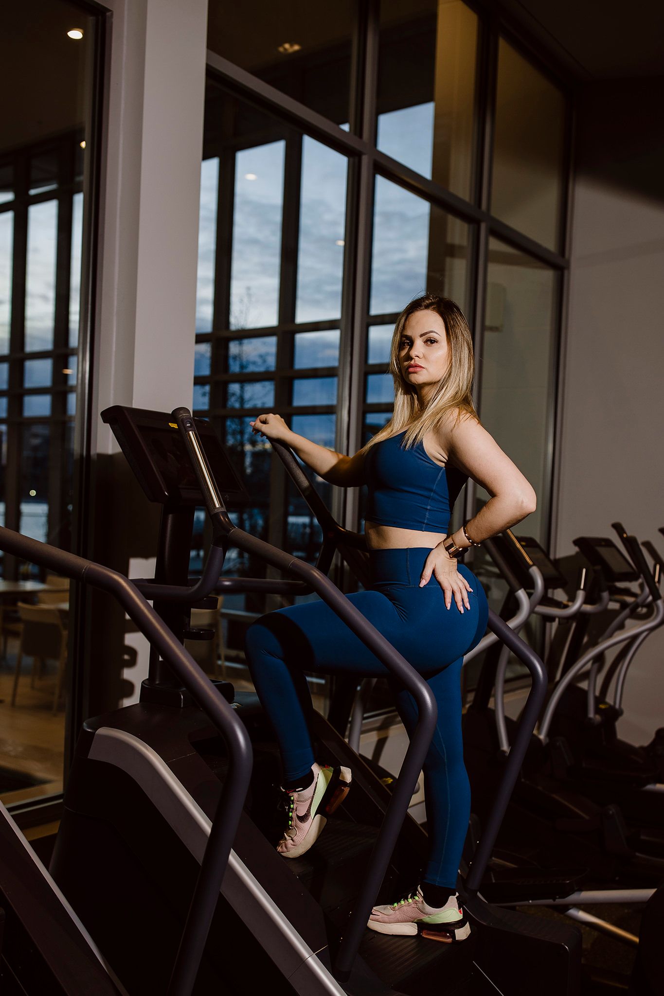 Athletic figure in blue workout set poses confidently on exercise equipment in gym setting.