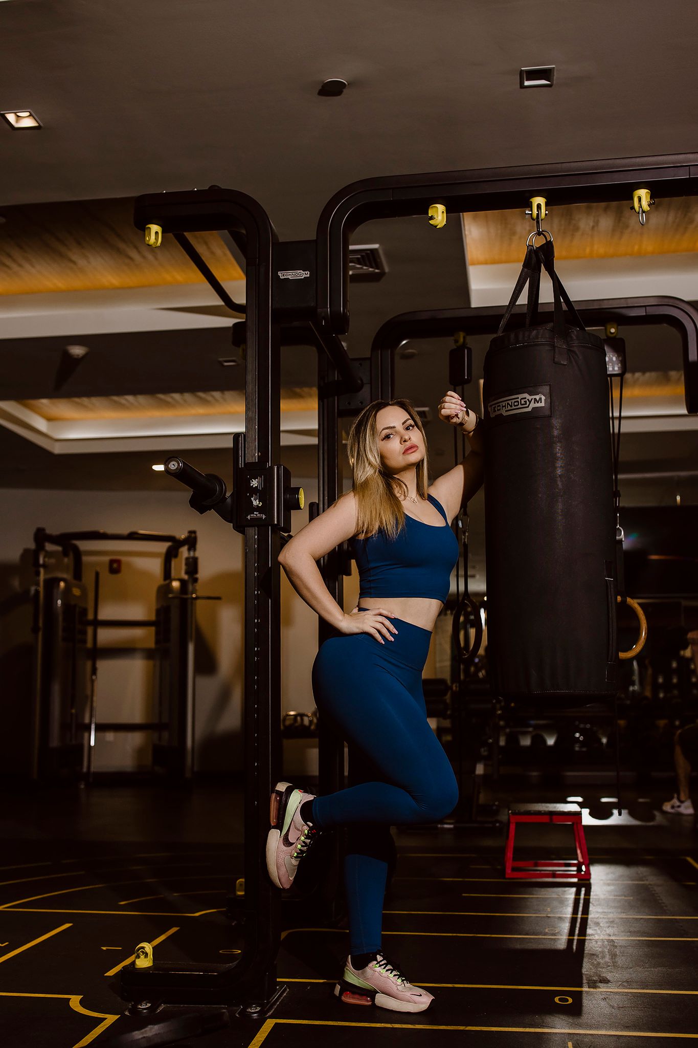 Fitness model in navy blue athletic wear poses confidently next to boxing equipment.