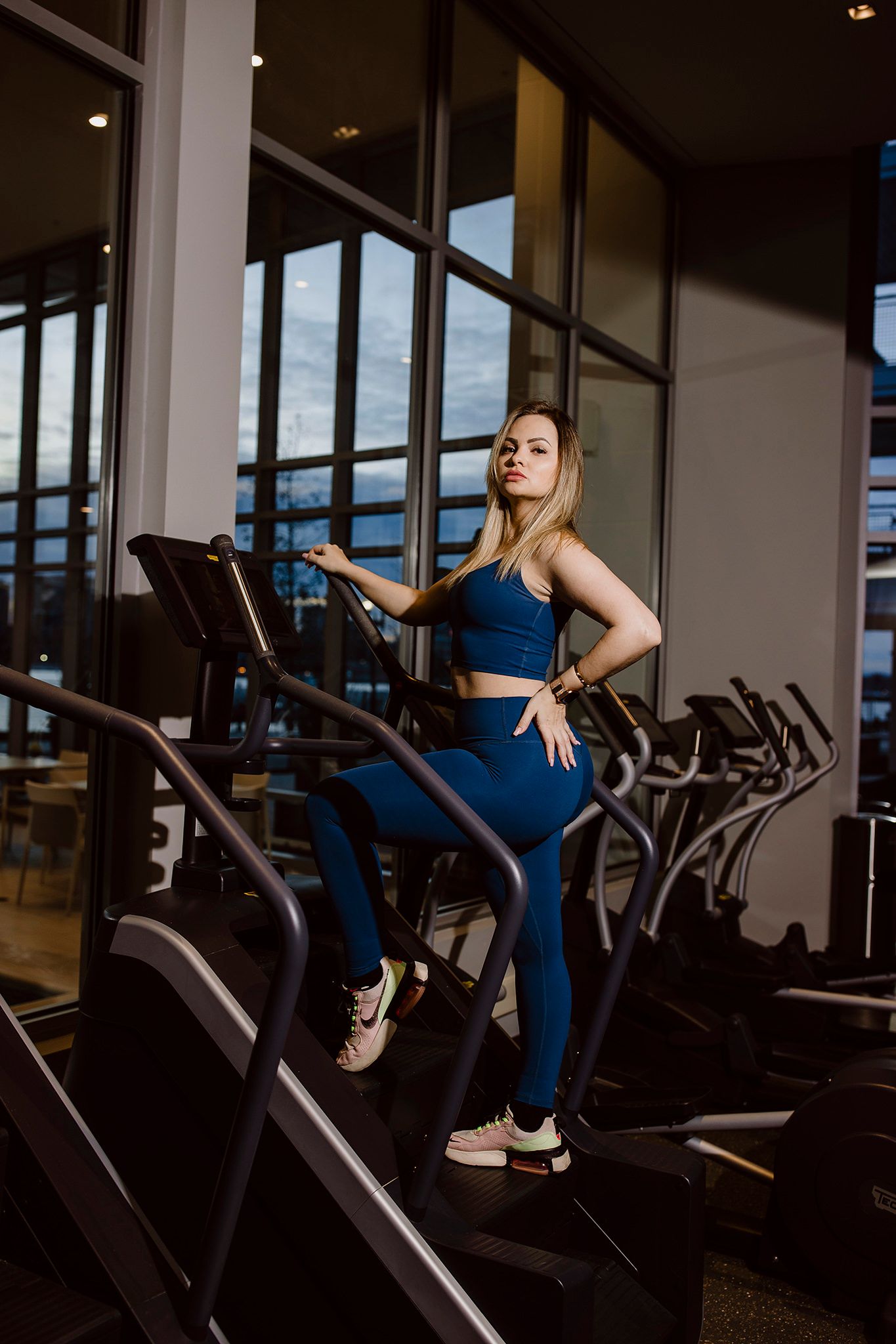 Woman in blue activewear demonstrates proper form on treadmill in modern fitness facility.
