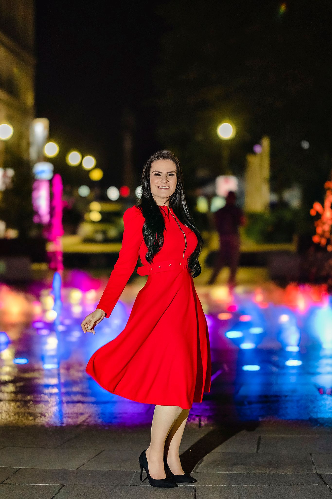 Red dress sparkles against colorful nighttime lighting and glowing orbs in an urban setting.