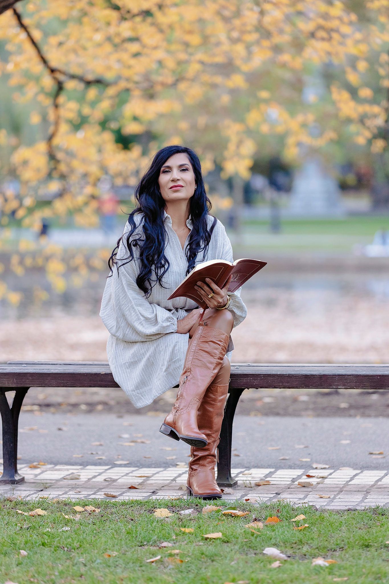 Person reading book on park bench surrounded by autumn foliage.